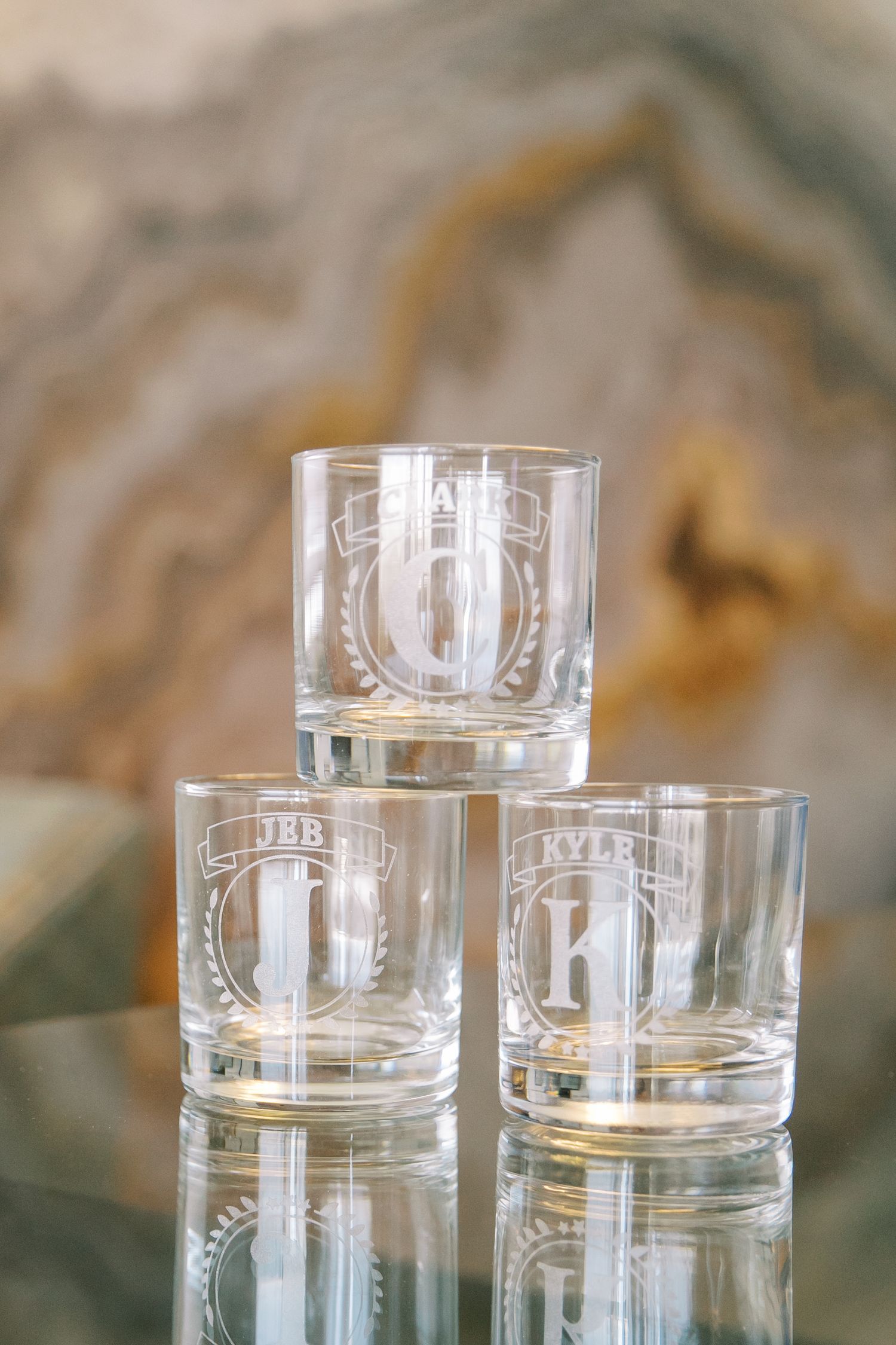 Three etched glass tumblers arranged in a pyramid formation against a marbled background.