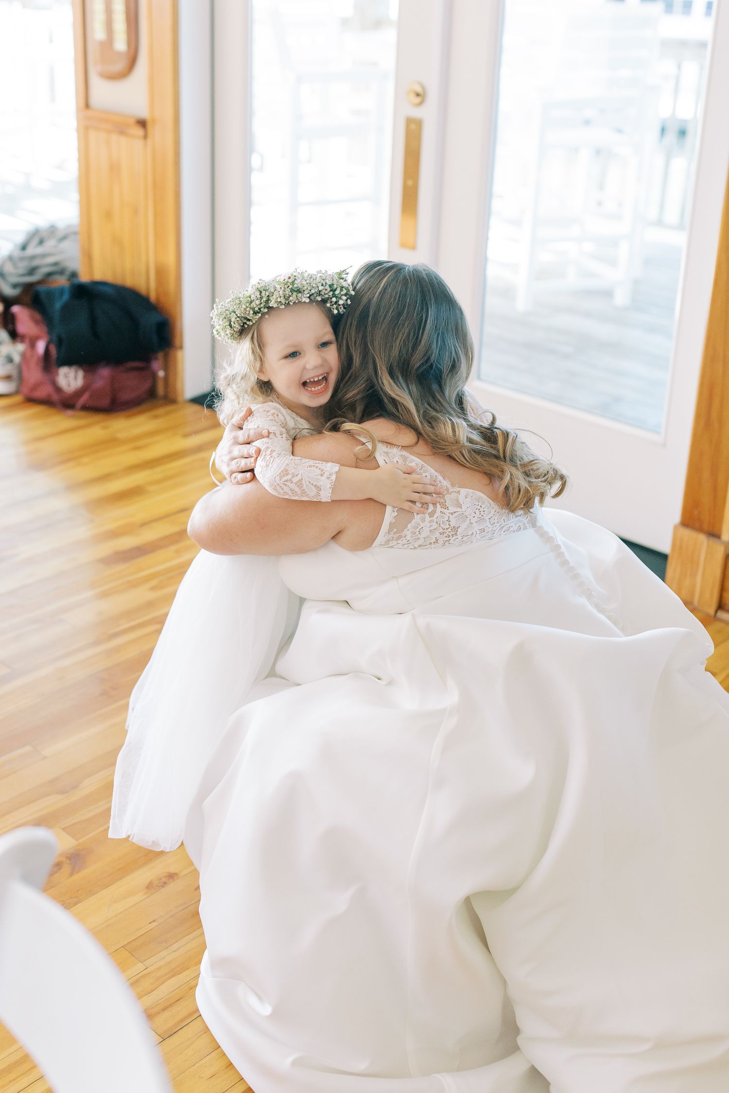 Sweet embrace between two people in white dresses on hardwood floors during wedding preparations.