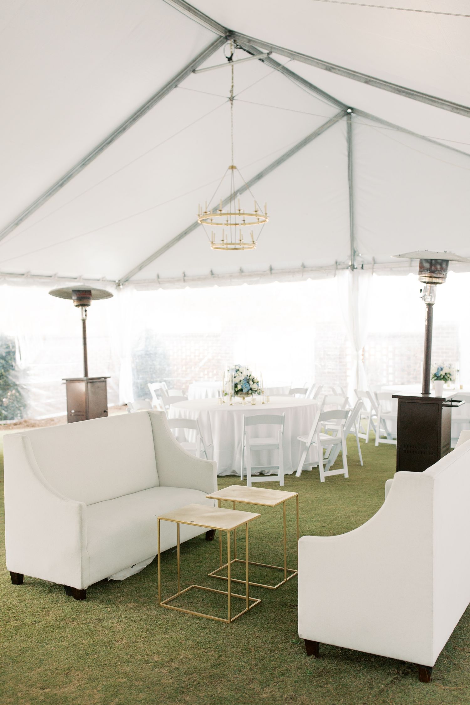Modern white tent reception setup with elegant lounge furniture and gold accents.