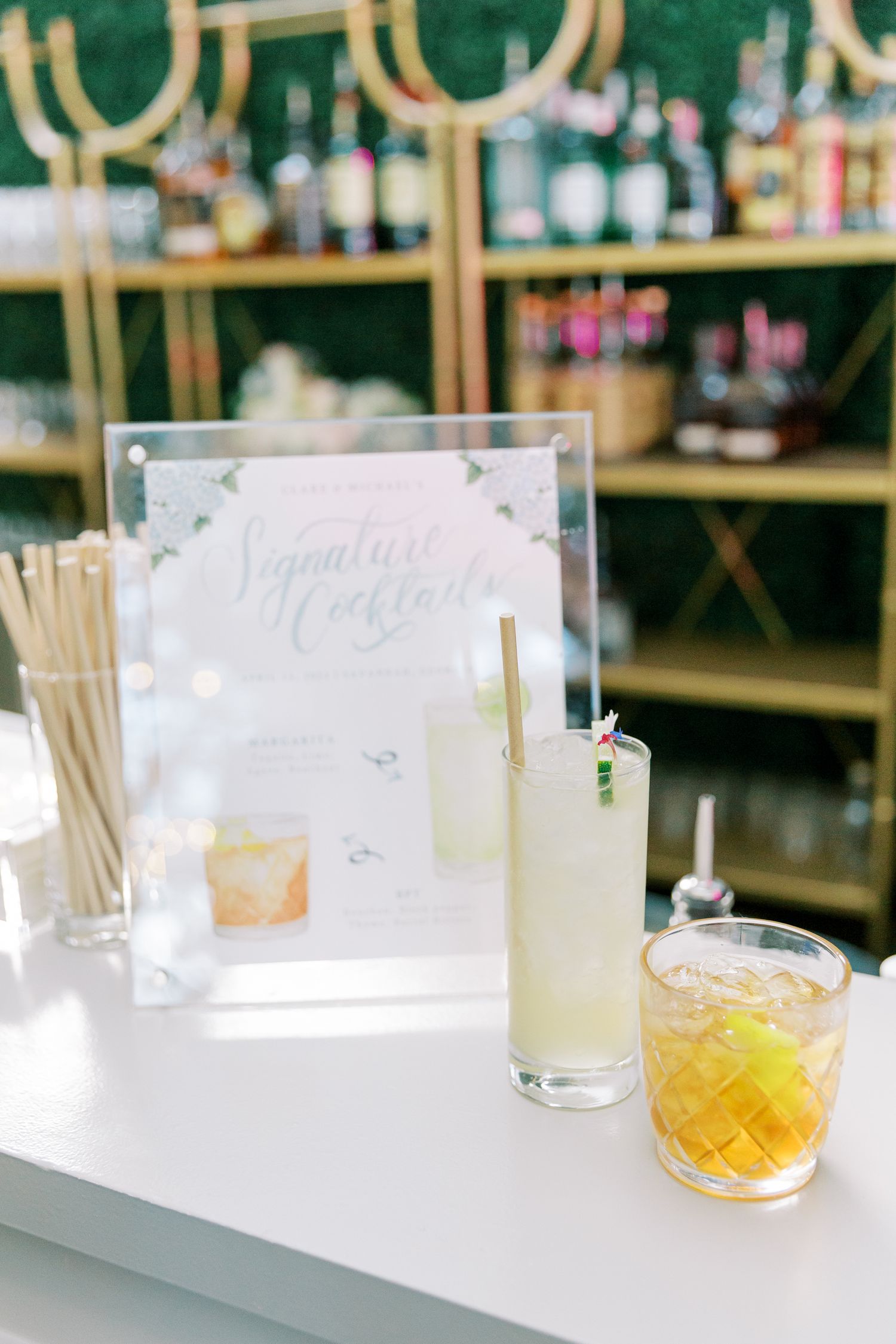 Wedding cocktail menu display with signature drinks on white bar counter.