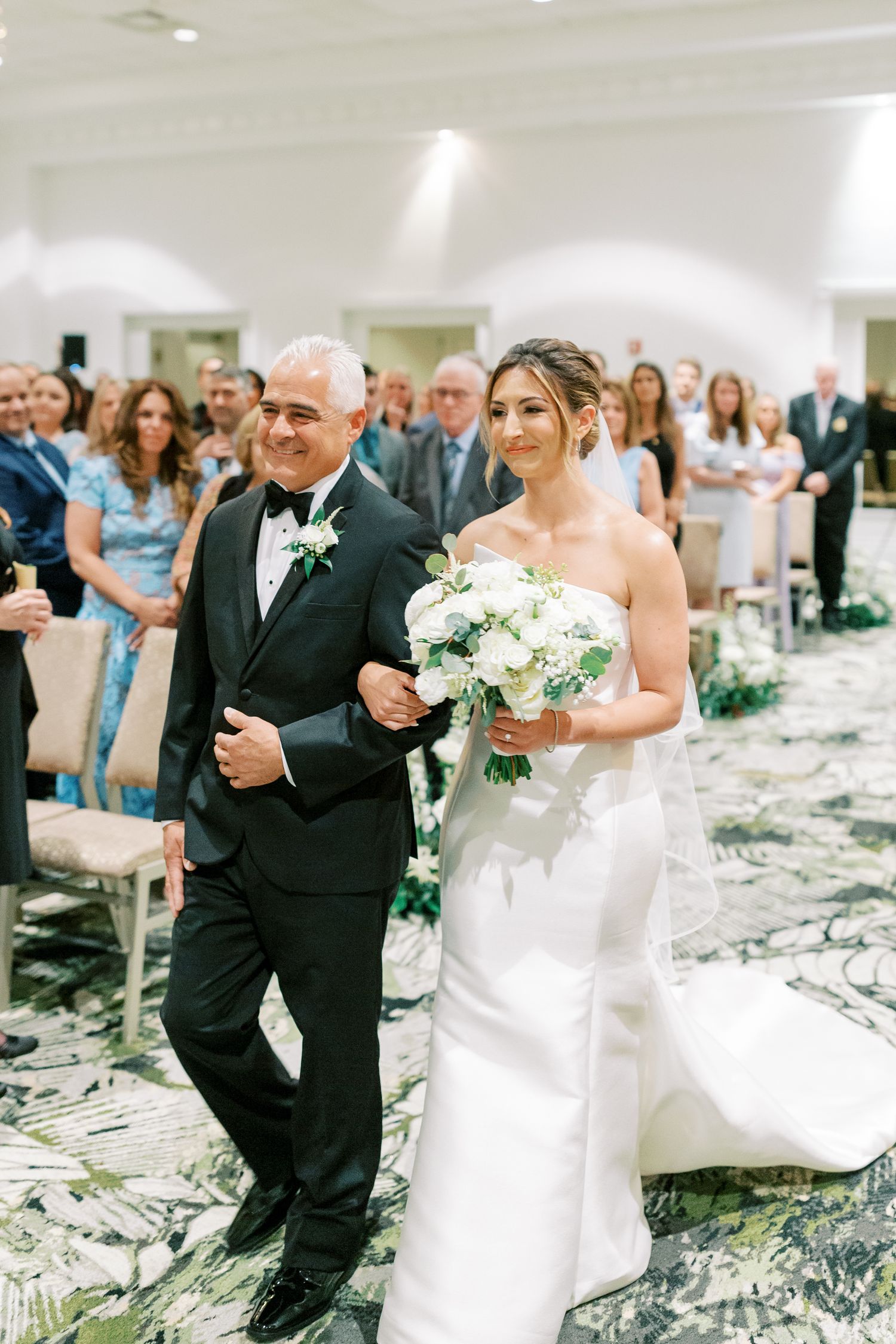 Wedding ceremony in an elegant indoor venue with floral aisle decorations.