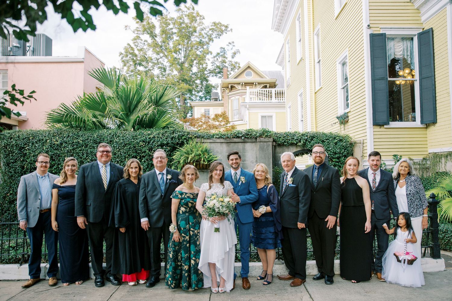 Wedding party group photo outside historic yellow house with traditional architecture.