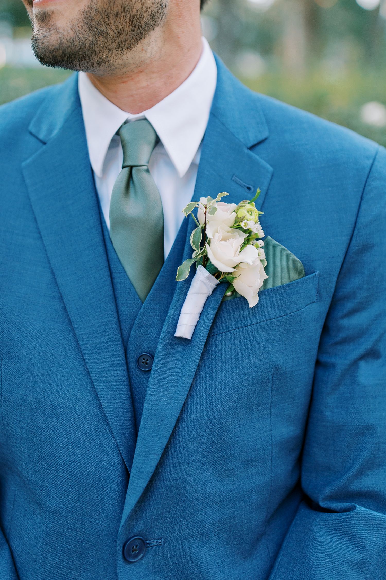 Groomsmen wearing bright blue suits with sage green ties and white boutonnieres.