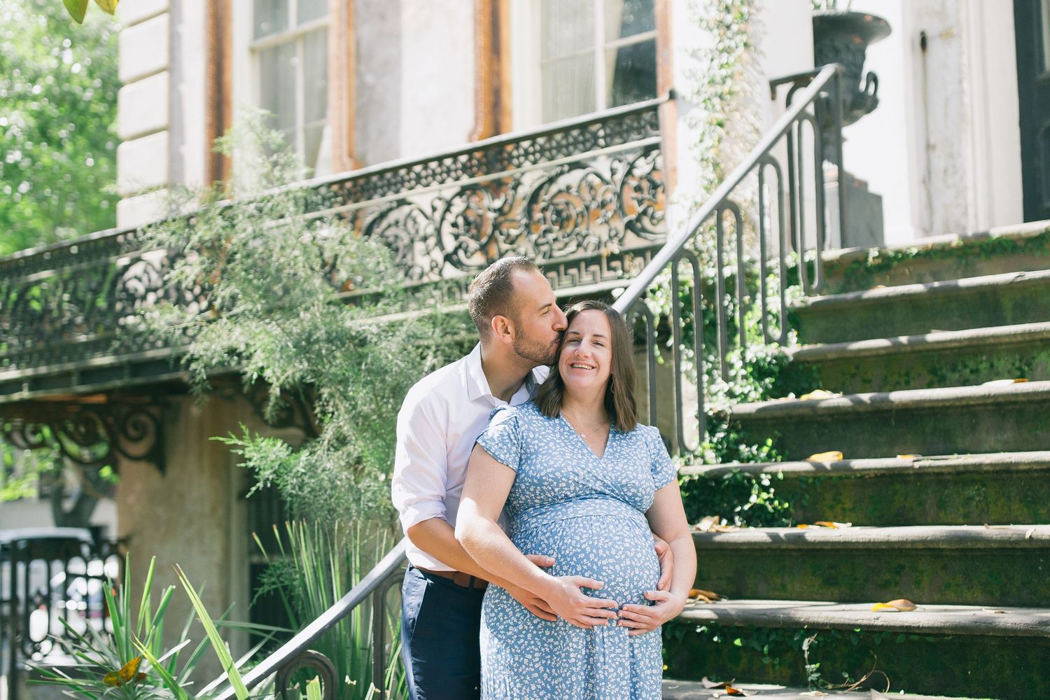 A couple poses together on rustic outdoor steps surrounded by lush greenery.