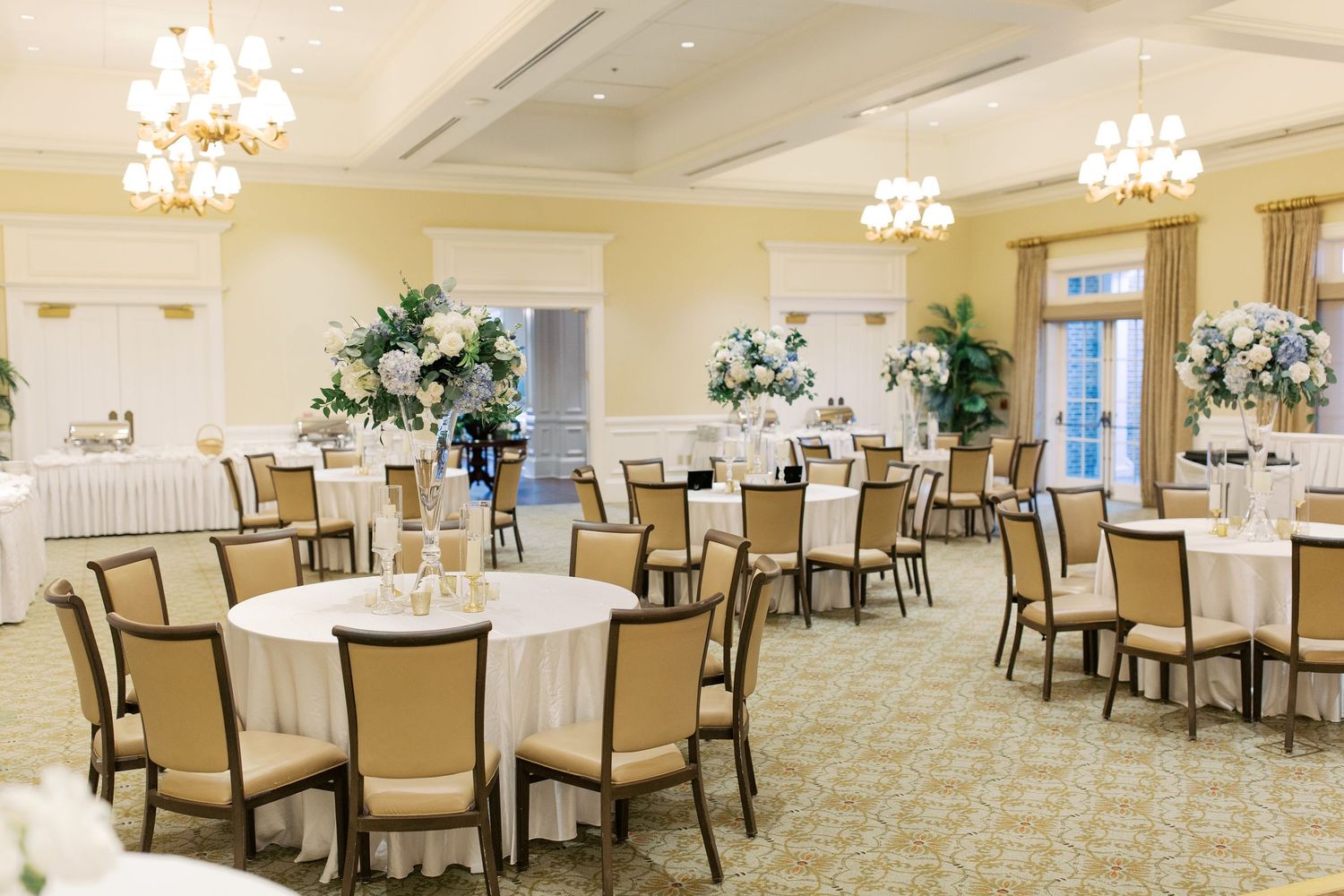 Elegant wedding reception room with round tables, cream chairs, and crystal chandeliers.