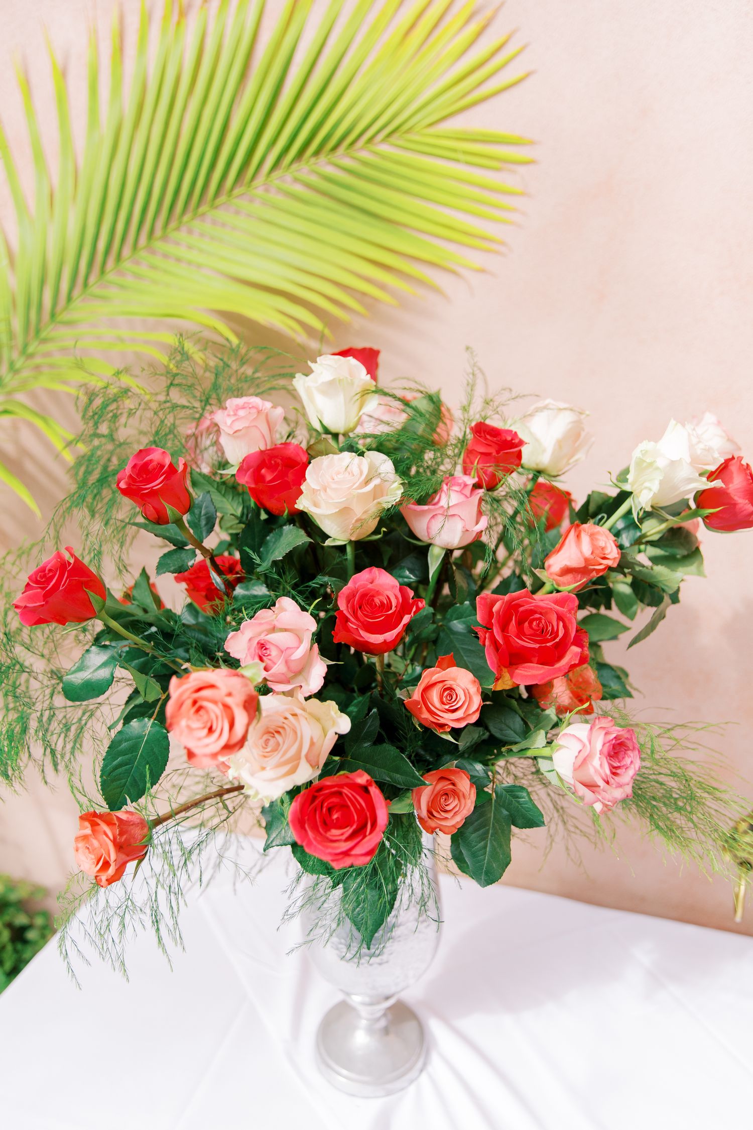 Beautiful floral arrangement of pink and red roses with palm leaves in an elegant white vase.
