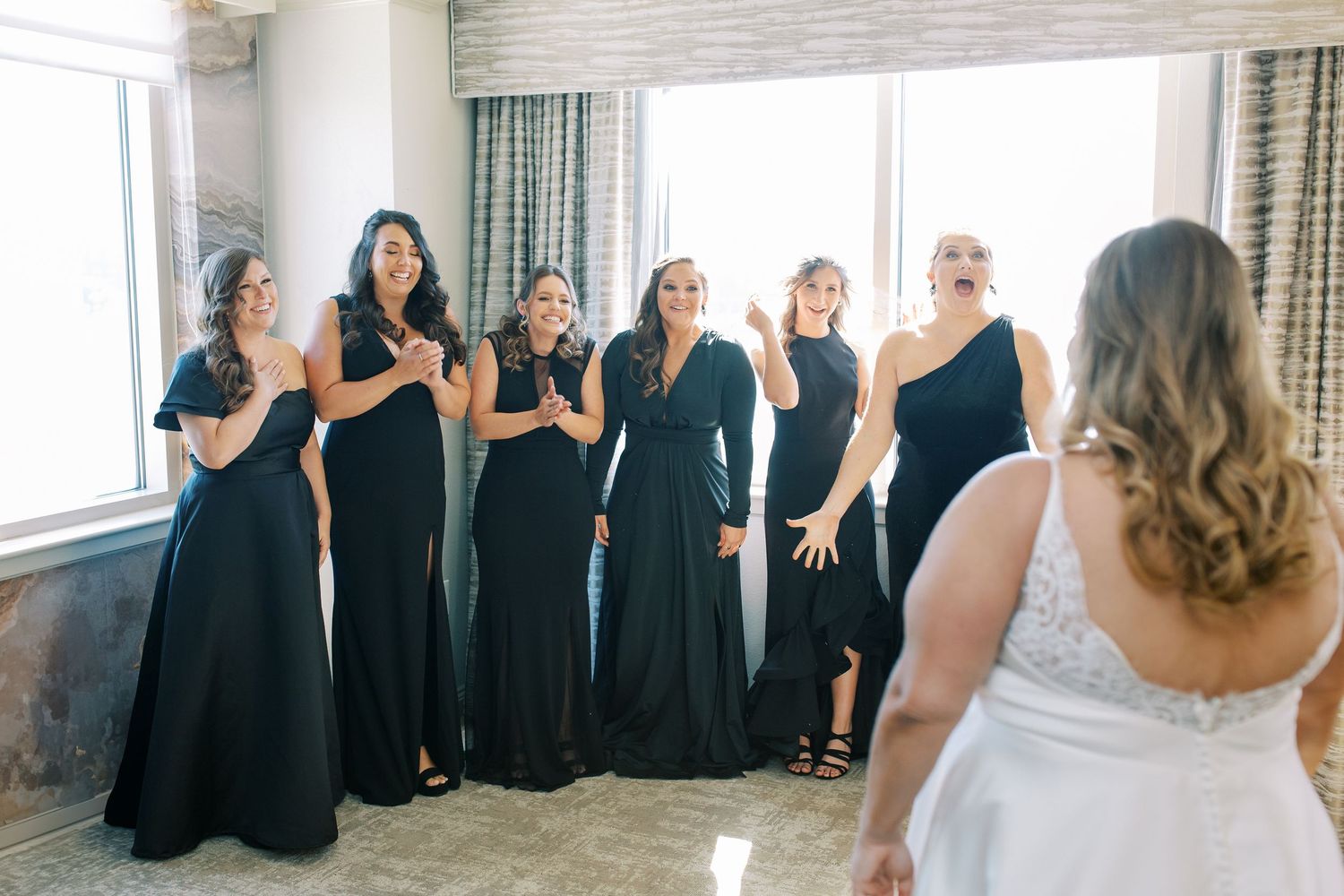 Bridesmaids in elegant black gowns react emotionally during a wedding reveal moment.