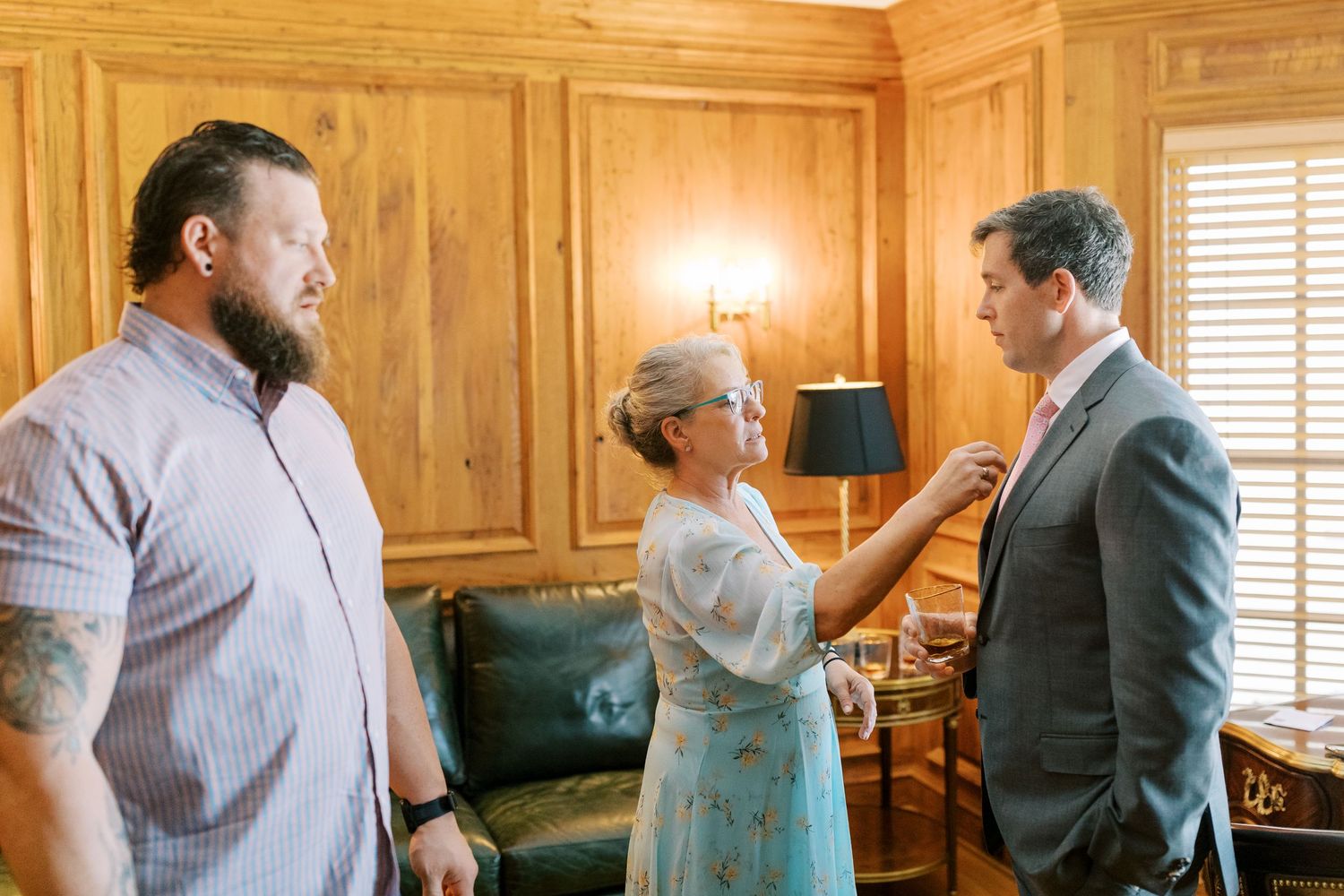 Three people having a conversation in a wood-paneled room with traditional decor and warm lighting.