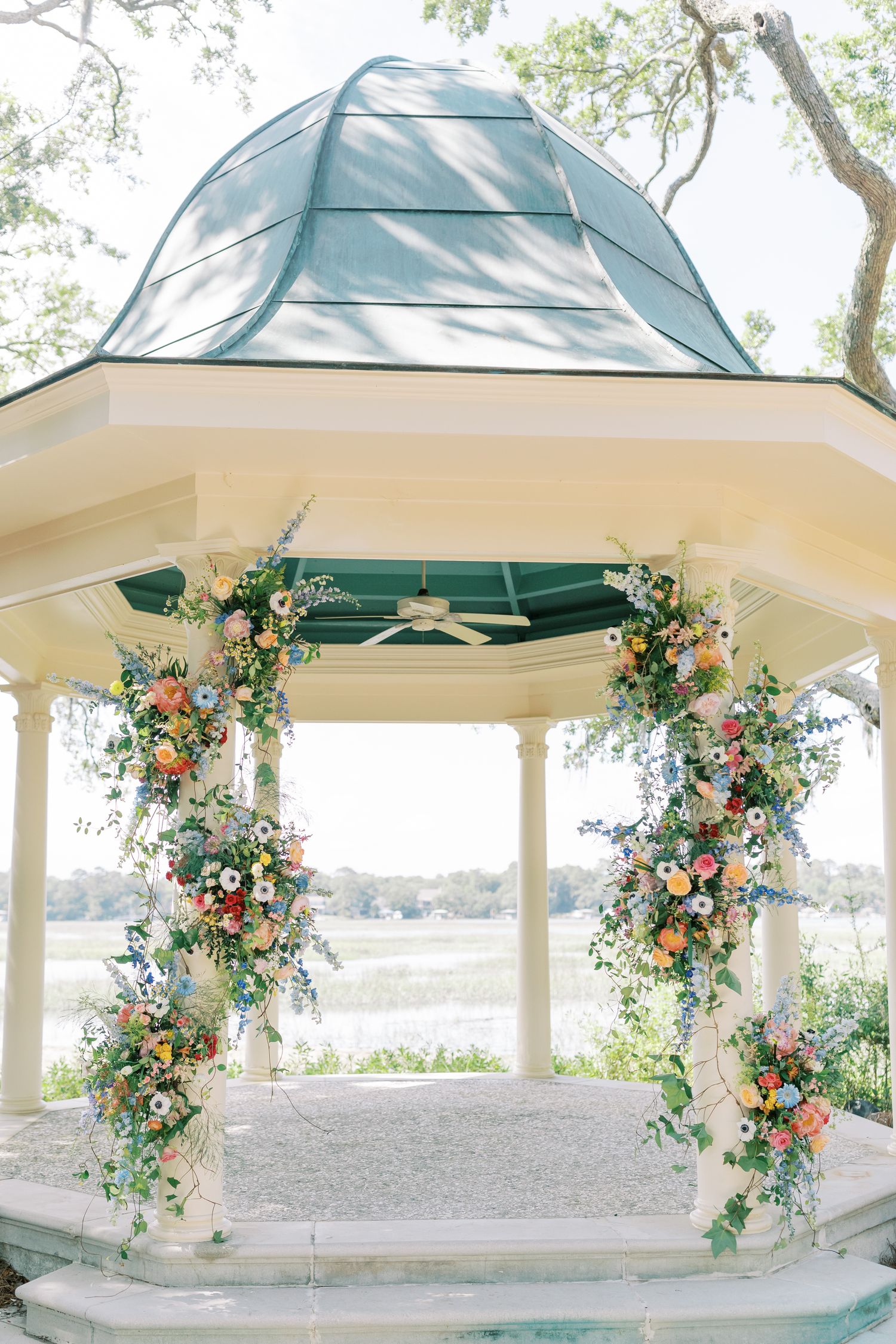 White gazebo decorated with cascading floral arrangements in peach and green for an outdoor wedding ceremony.