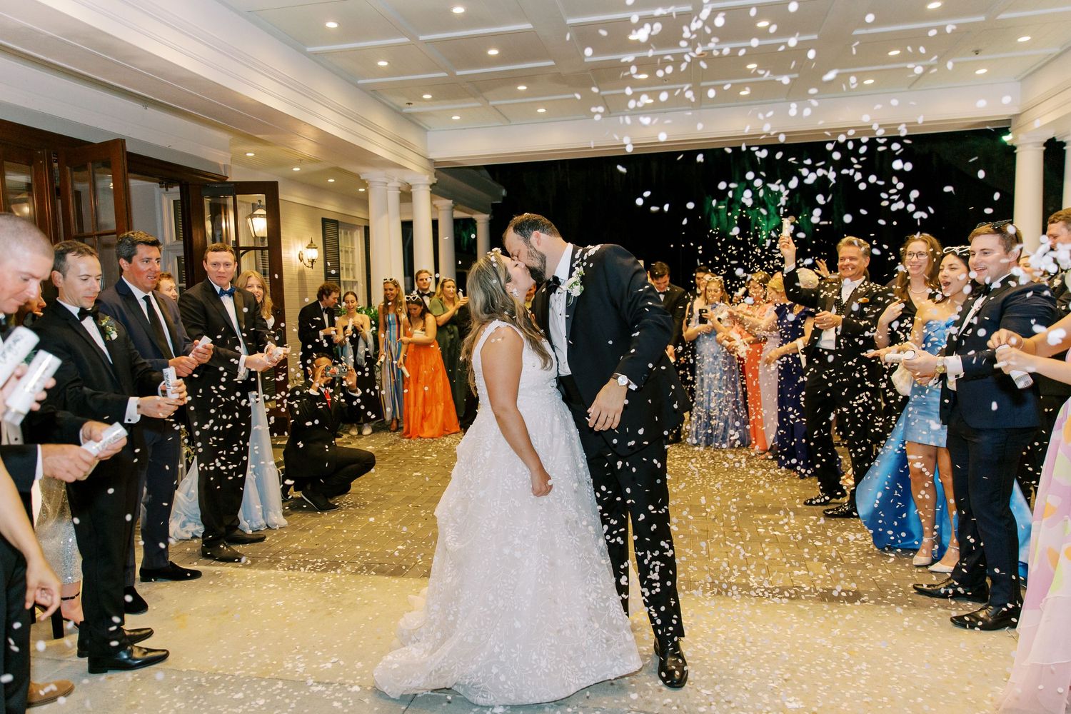 Wedding couple shares first dance under sparkling confetti while guests look on at elegant indoor reception.