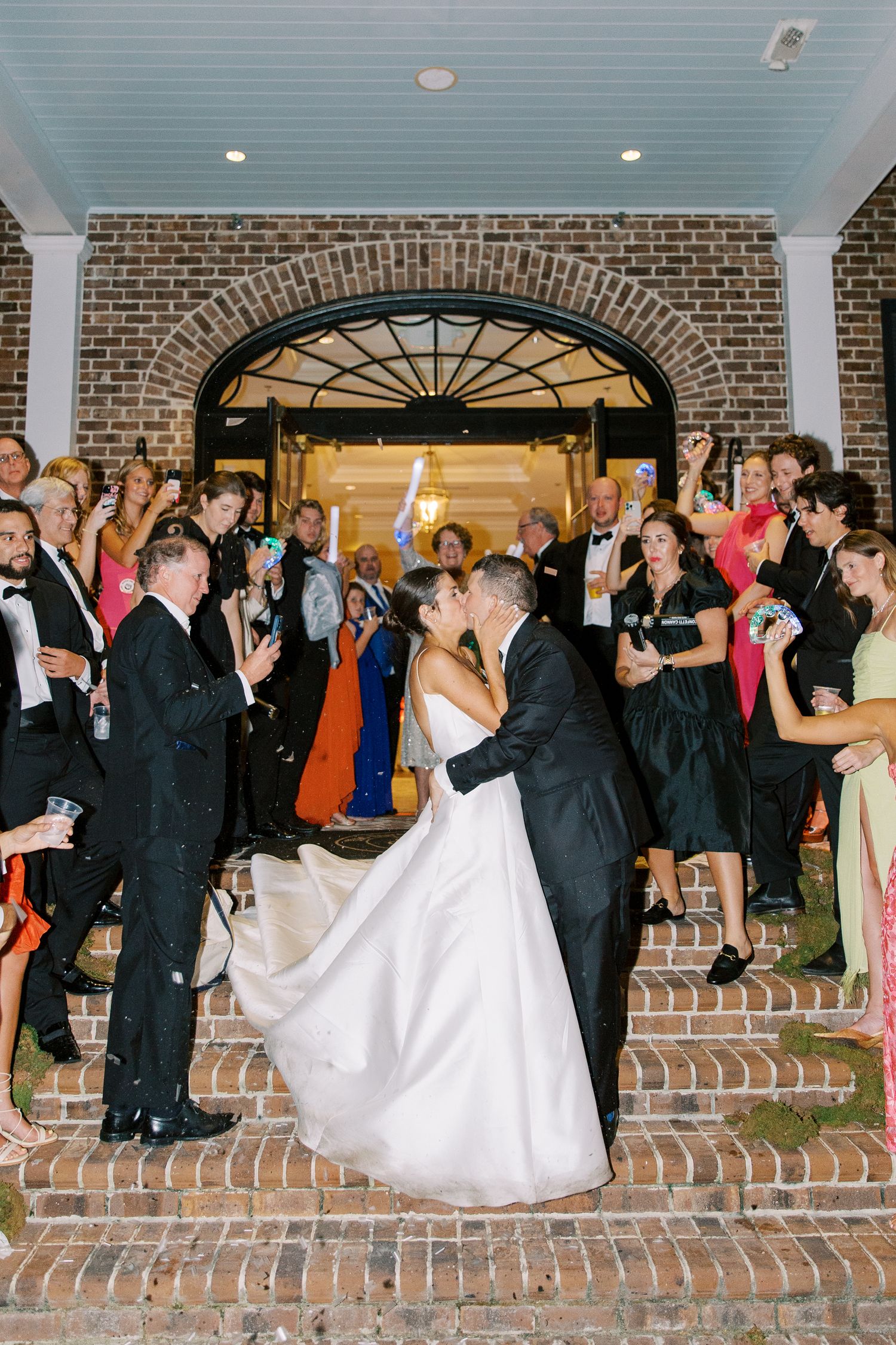 Wedding guests wave sparklers during a grand exit near a brick archway entrance at The Savannah Golf Club.