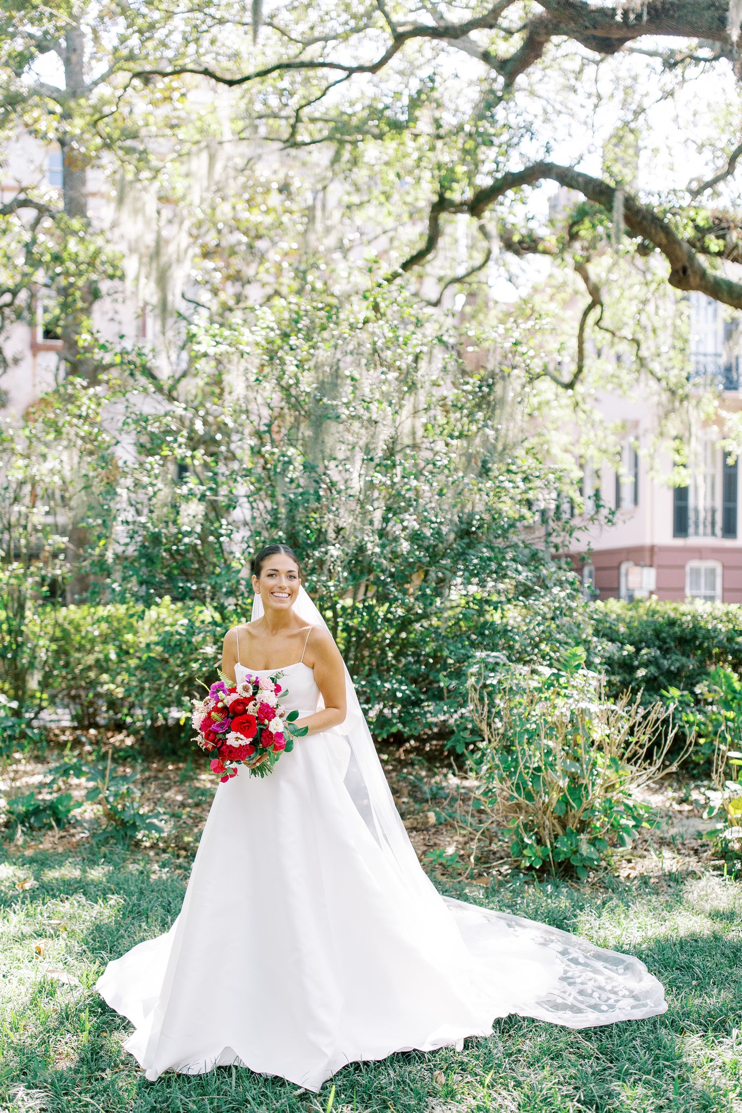 A bride in a strapless ball gown poses in a garden with Spanish moss trees.