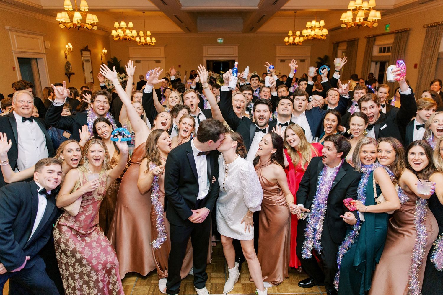 An energetic wedding reception crowd cheering and celebrating in an ornately lit ballroom.