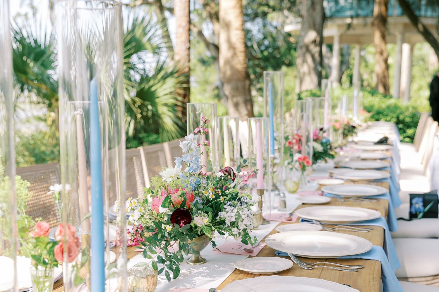 An elegantly set wedding reception table with blue accents and floral centerpieces outdoors.