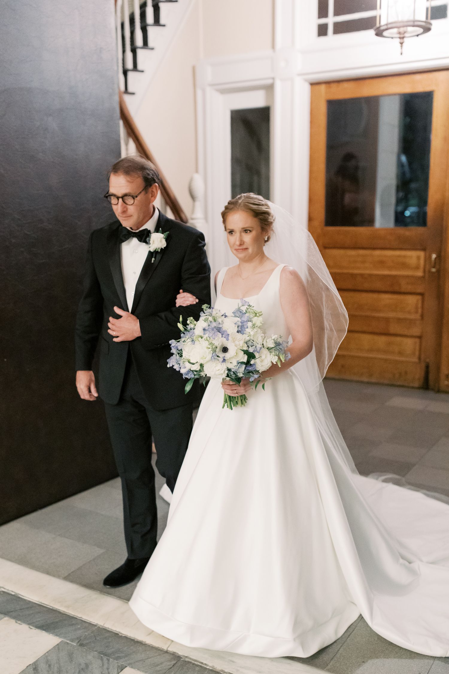 A classic wedding portrait featuring a white ball gown with delicate floral bouquet in an elegant indoor setting.