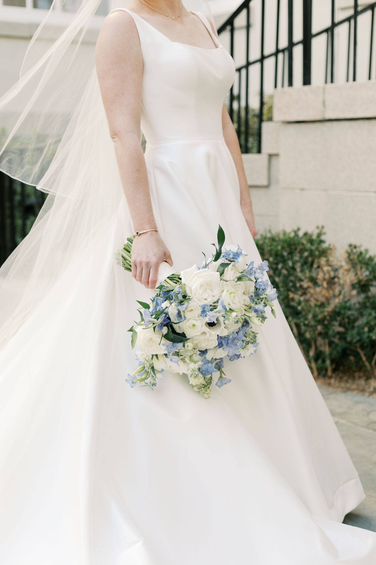 Close-up of white wedding dress details with blue and white bridal bouquet.