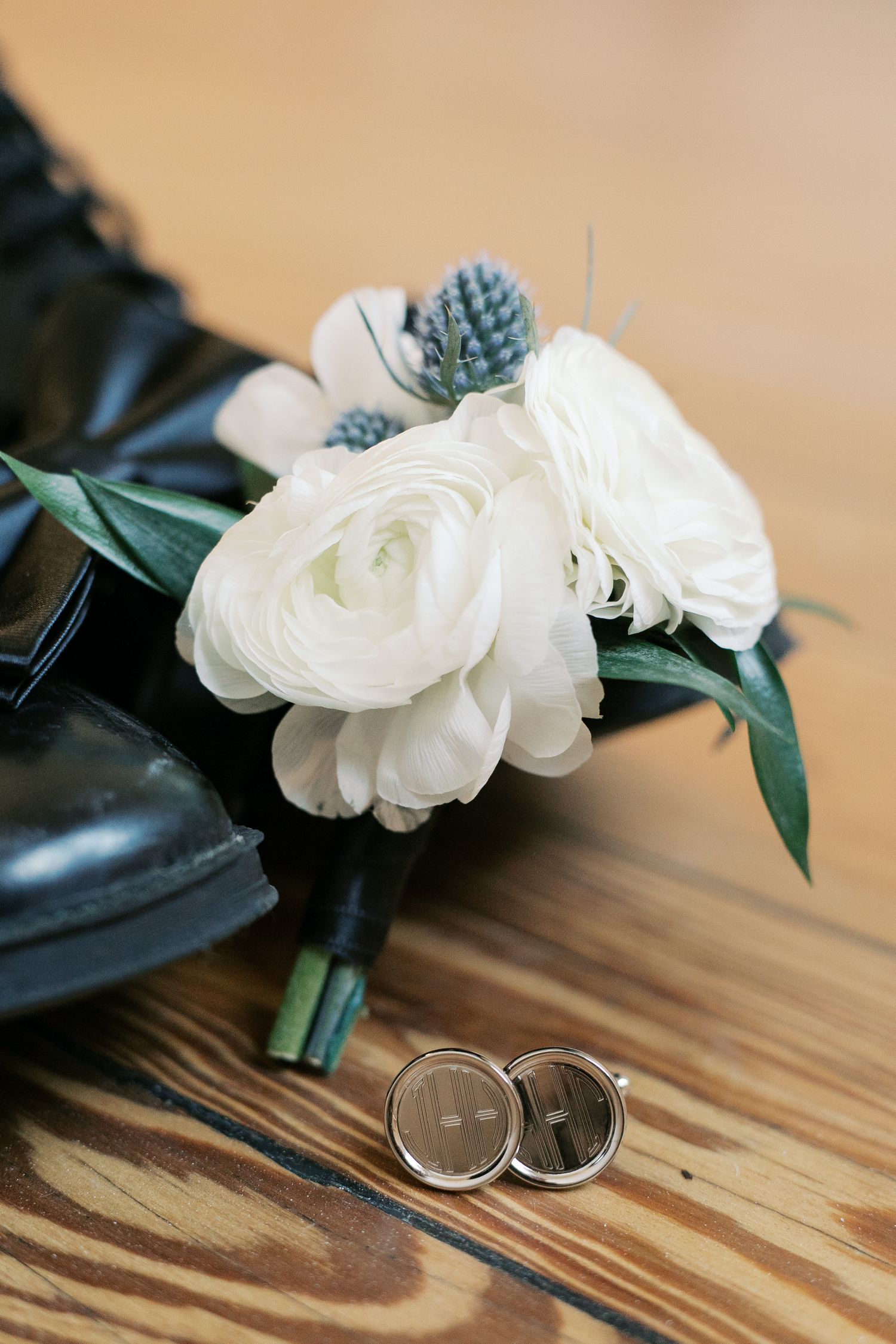 White ranunculus boutonniere with greenery next to wedding rings on wooden surface.