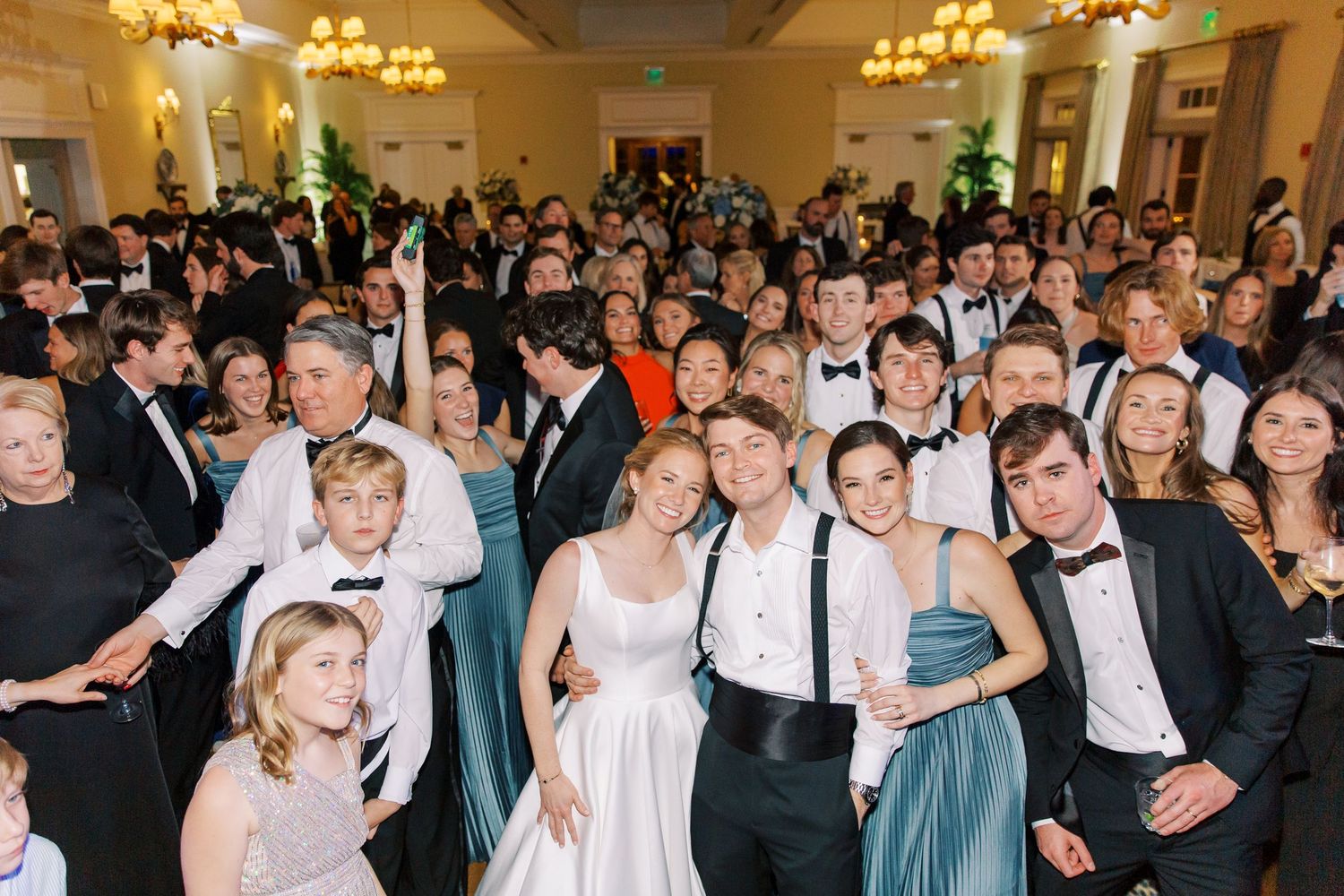 Crowded wedding reception with guests in formal attire dancing and celebrating.