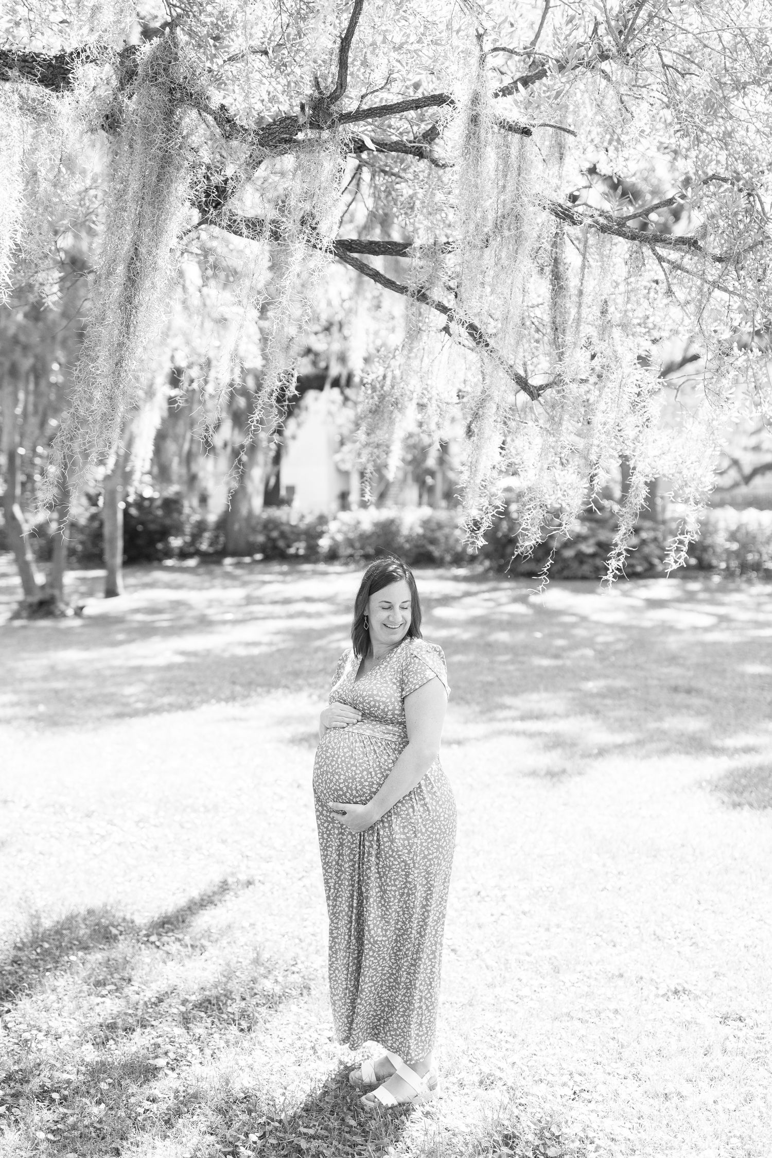 Black and white maternity photos showing expecting mother in flowing dress against sunlit outdoor setting.