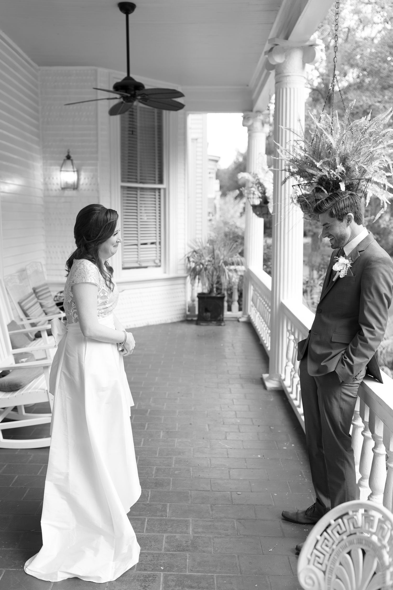 Black and white photo of a wedding moment on a traditional Southern porch with rocking chairs.