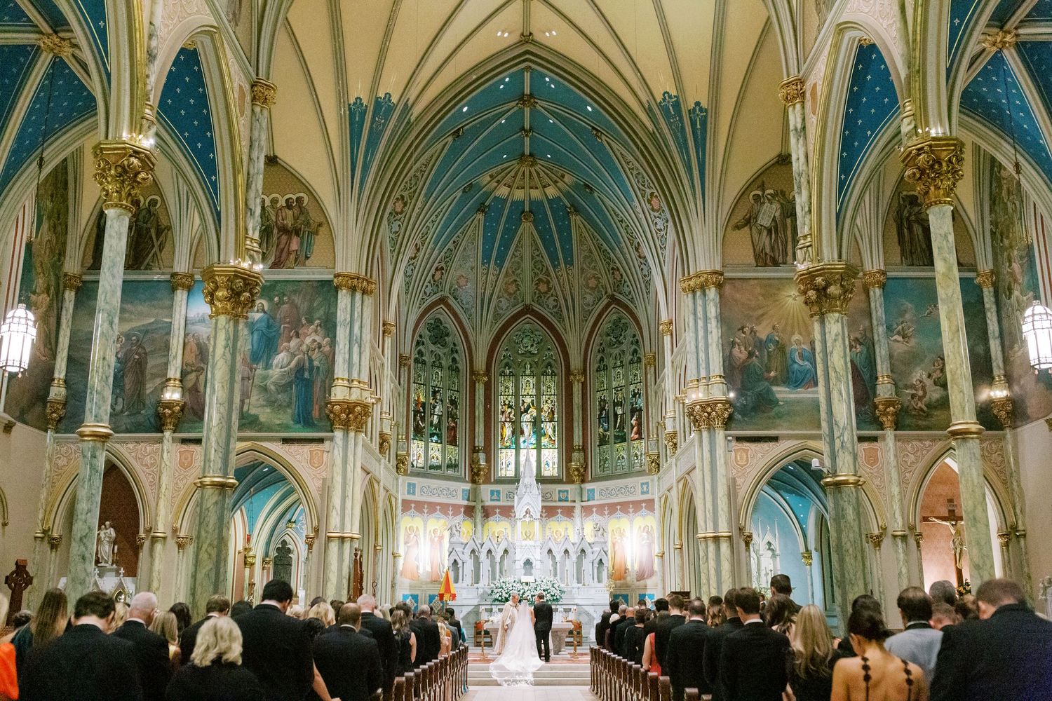 Cathedral wedding ceremony with gothic architecture and stained glass windows at the Cathedral of St. John the Baptist in Savannah, GA.