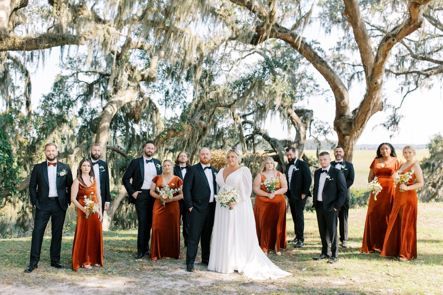 Wedding party in formal attire standing beneath old oak trees with Spanish moss.