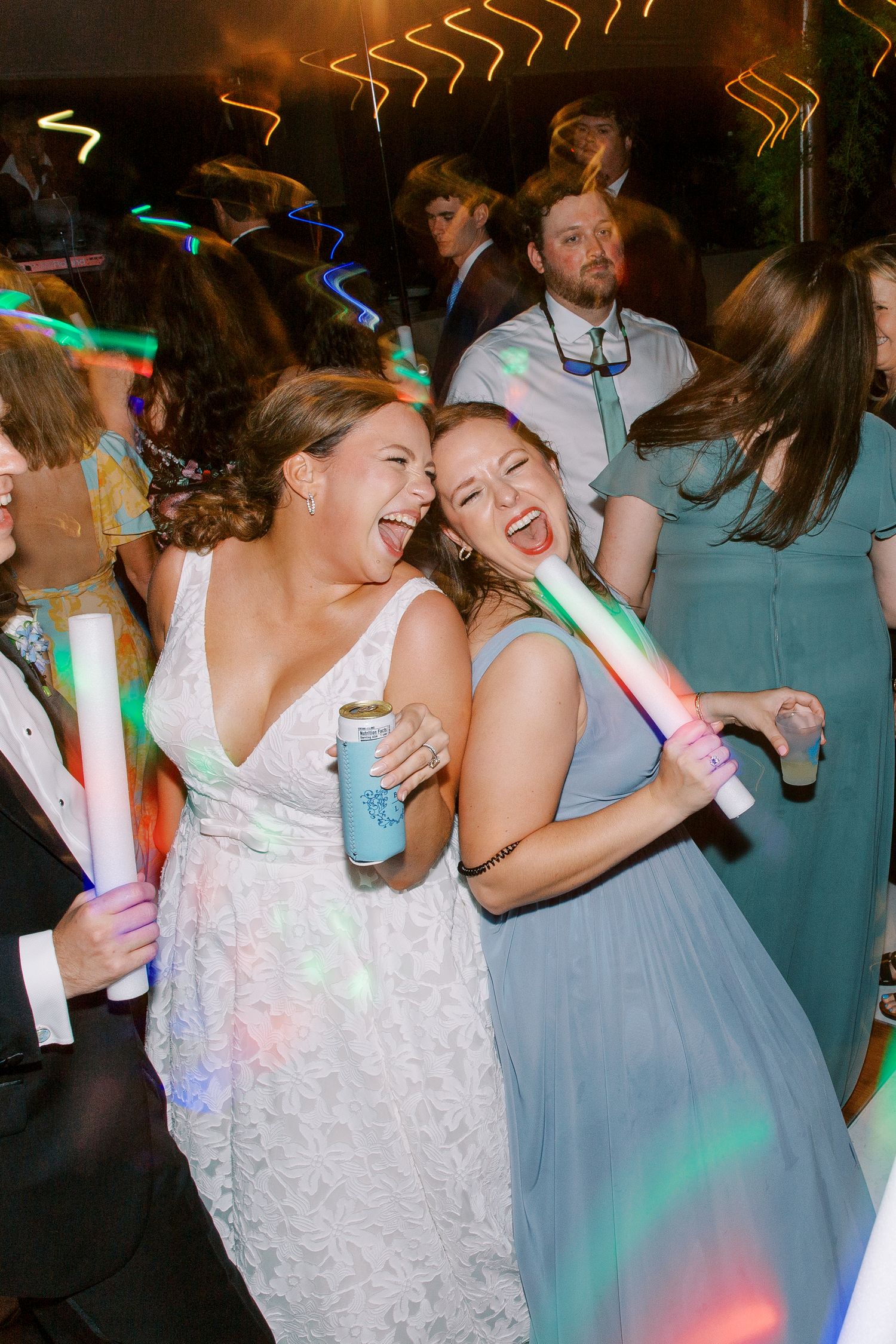 Wedding guests dancing and celebrating on the dance floor with colorful LED light sticks.