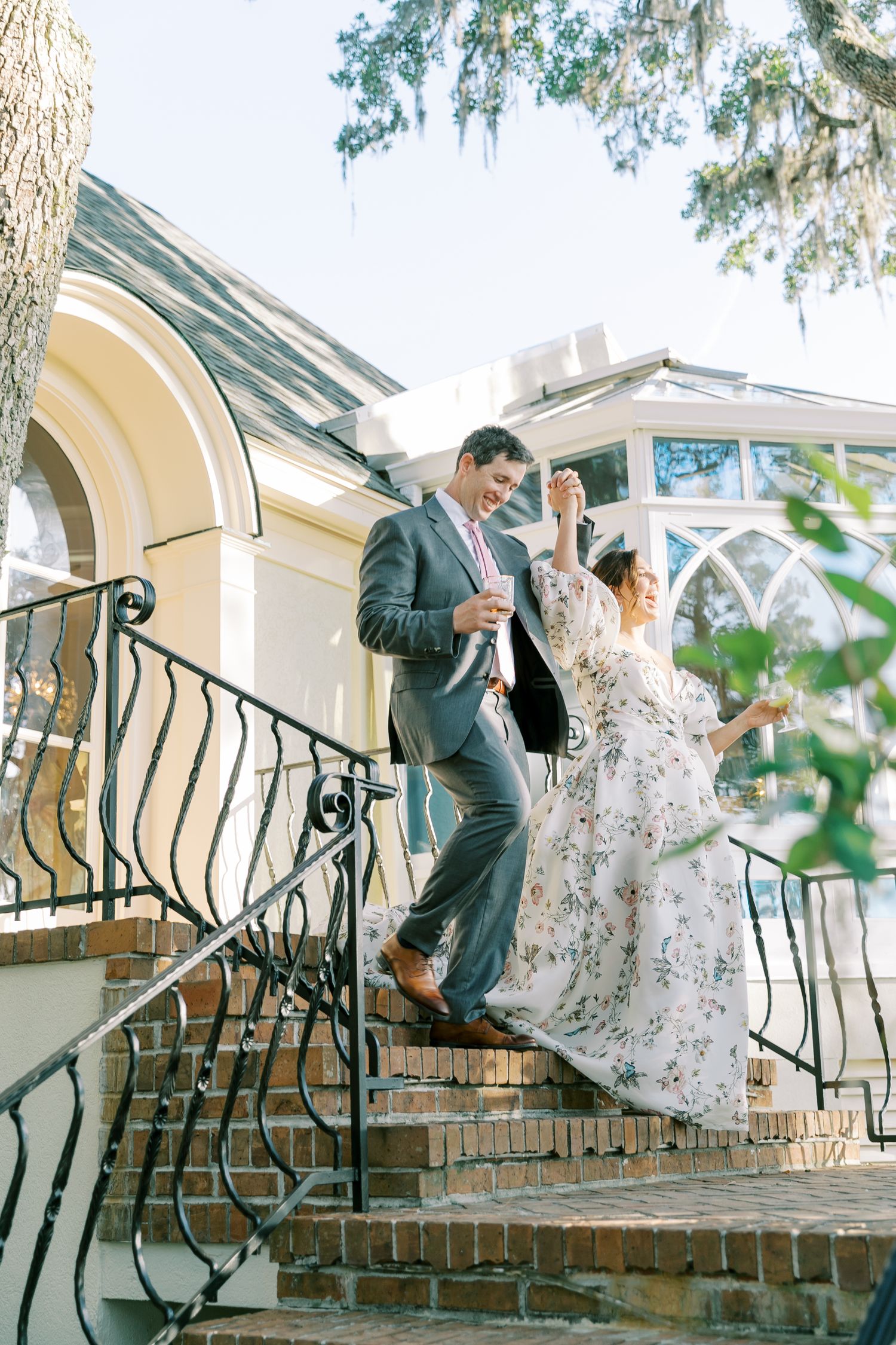 A couple poses on outdoor stone steps with decorative wrought iron railings at an elegant venue.
