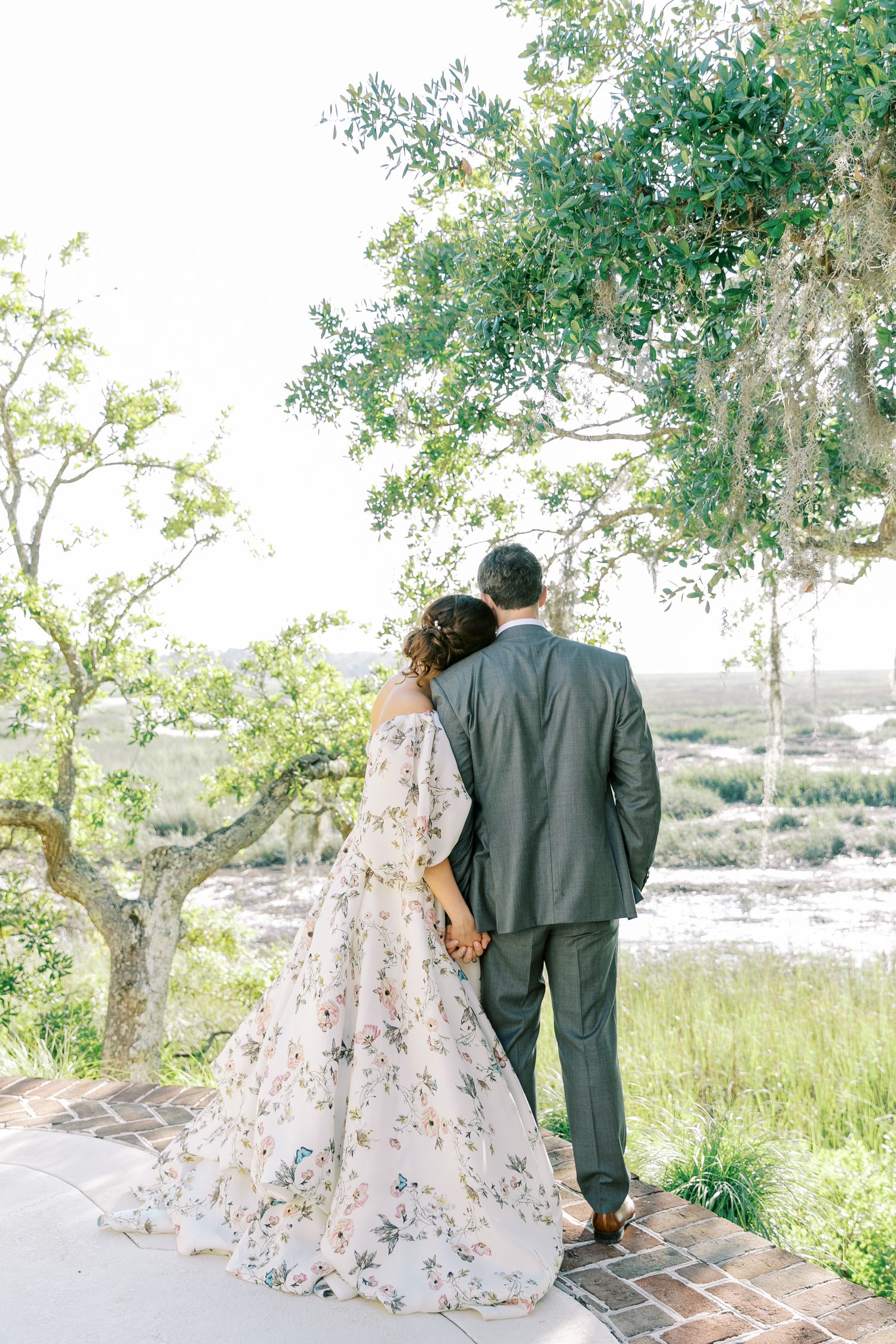 A couple in wedding attire looking out over a scenic landscape from a brick pathway.
