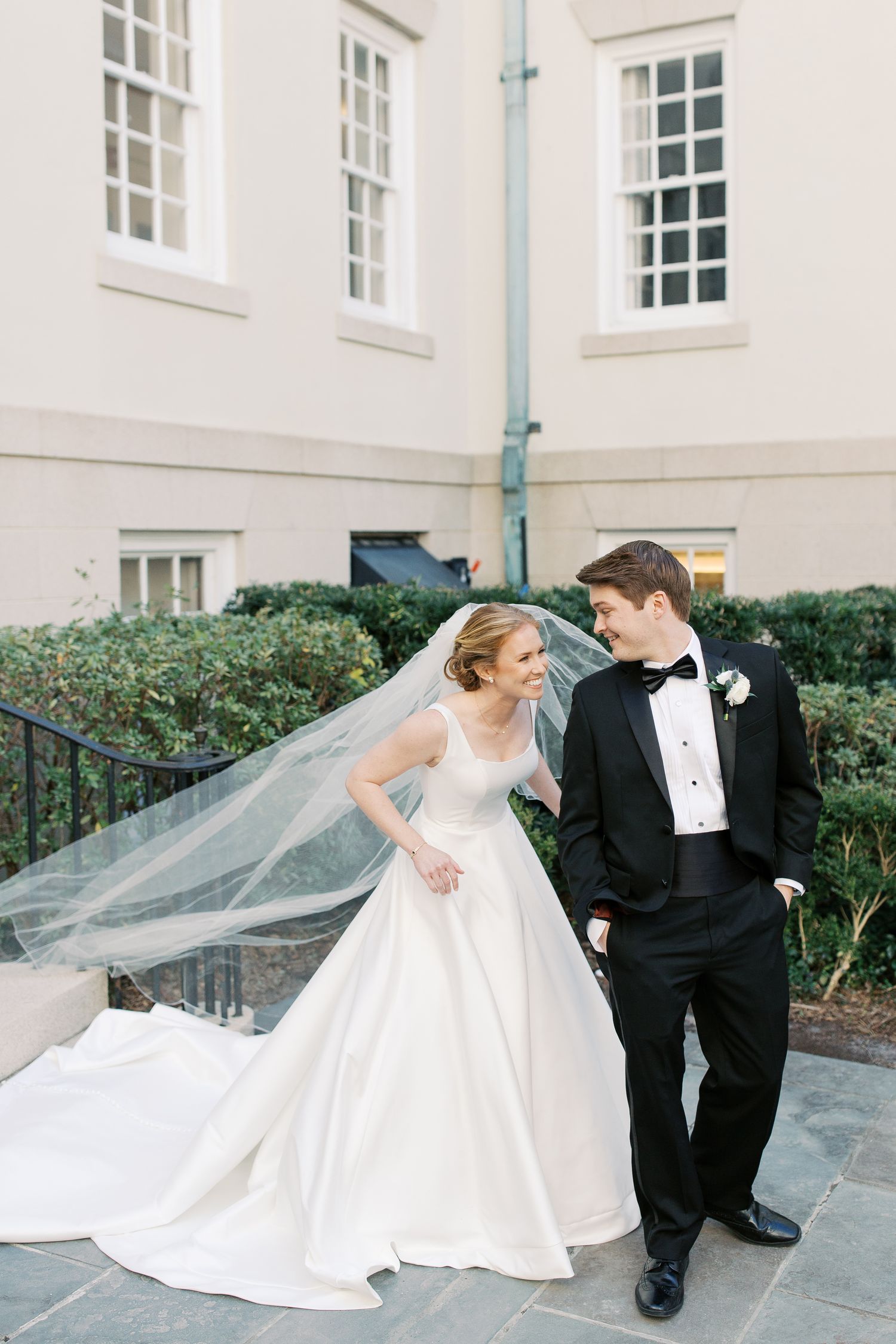 Elegant wedding couple poses together in a series of romantic shots against a white building exterior.