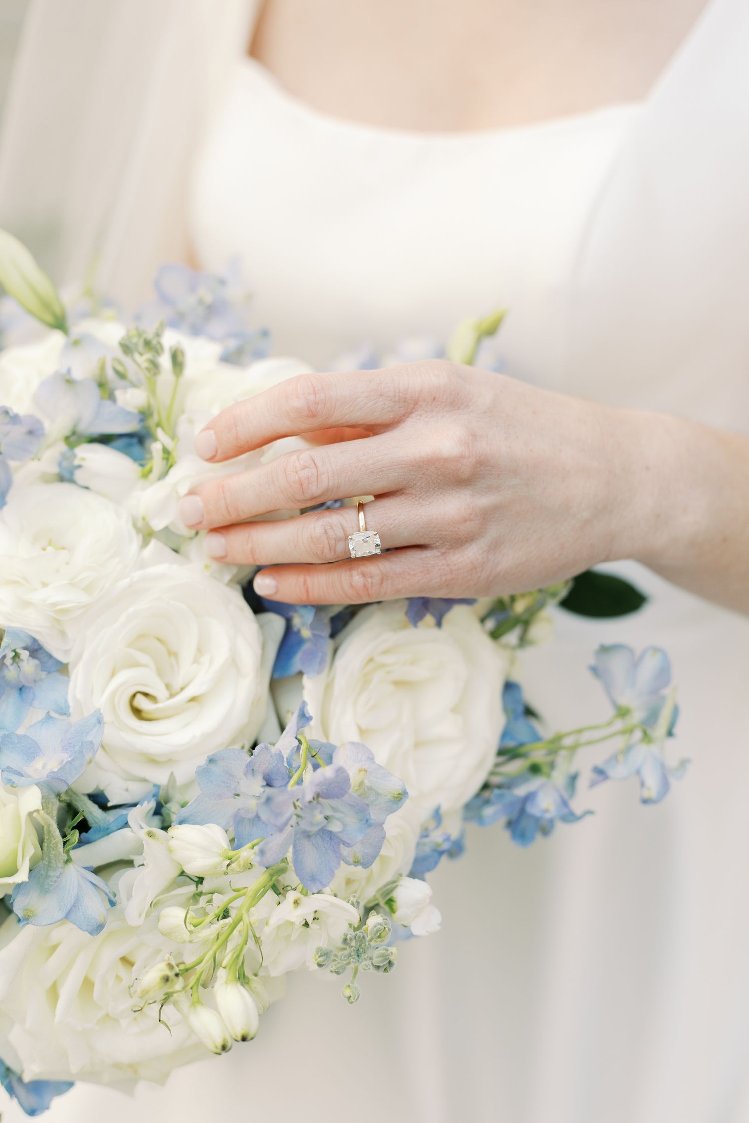 A delicate white and blue wedding bouquet with roses and an engagement ring on display.