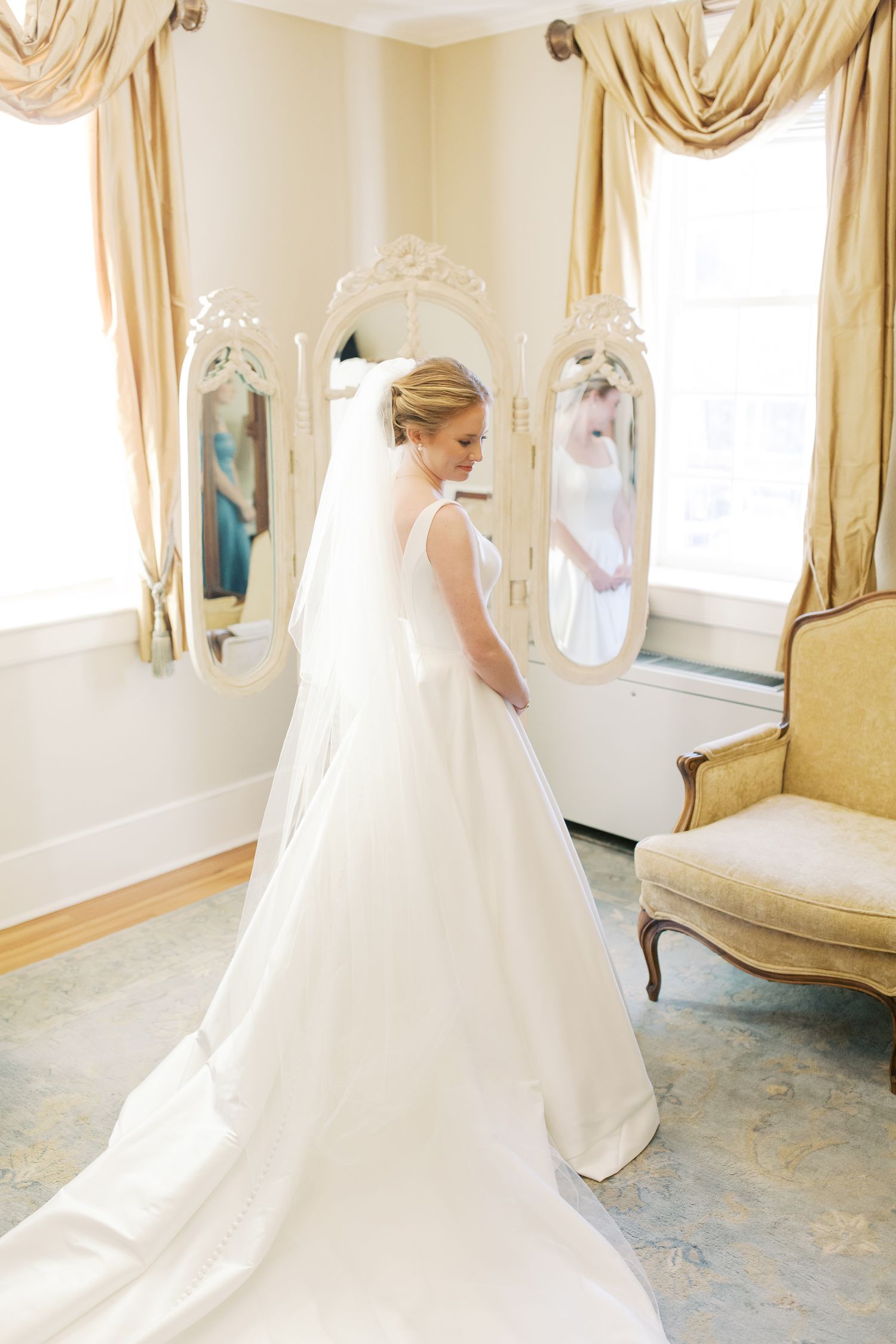 A bride in a classic white ball gown with cathedral train twirls in an elegant dressing room with draped curtains.