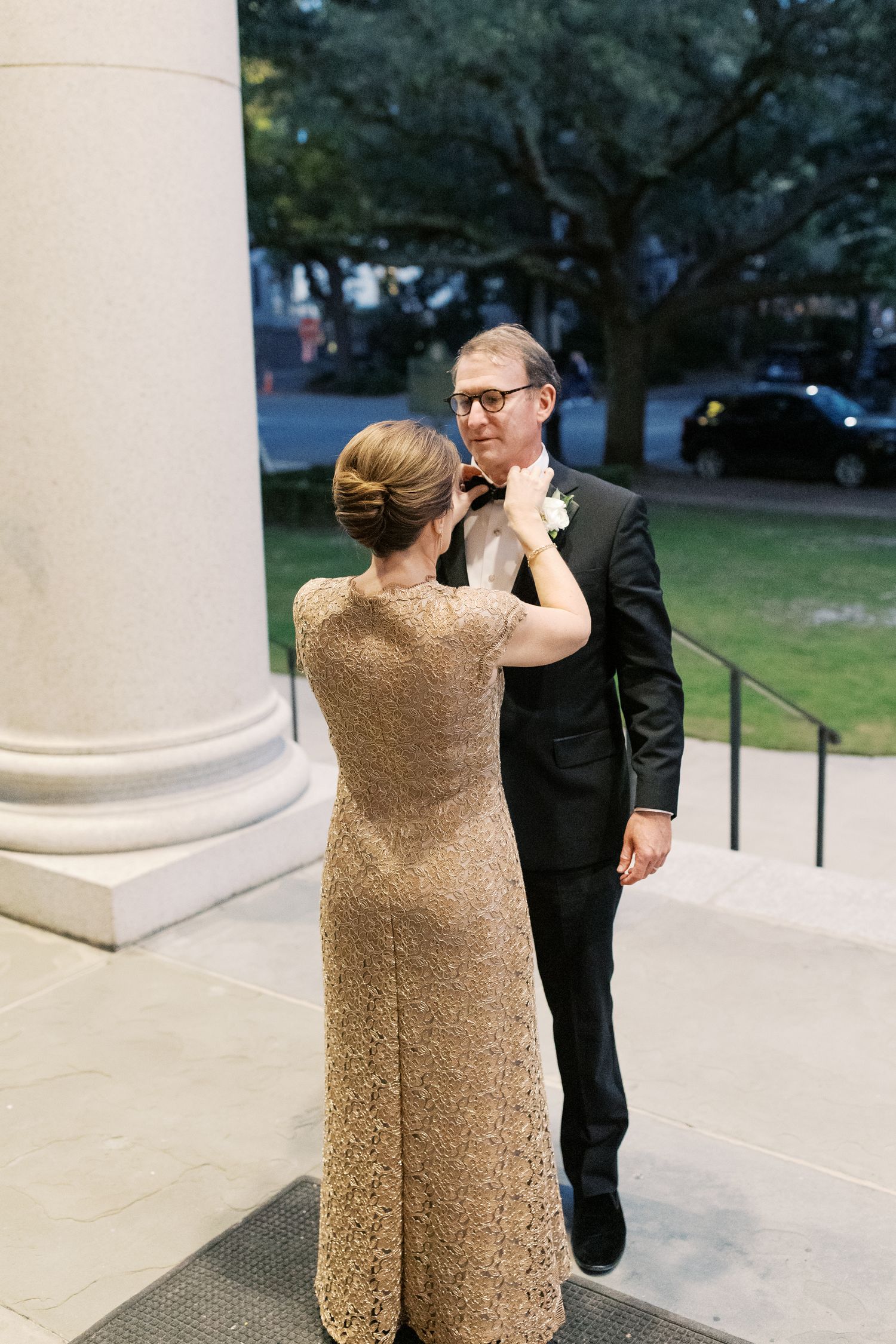 A touching moment between wedding guests outside a columned building entrance.