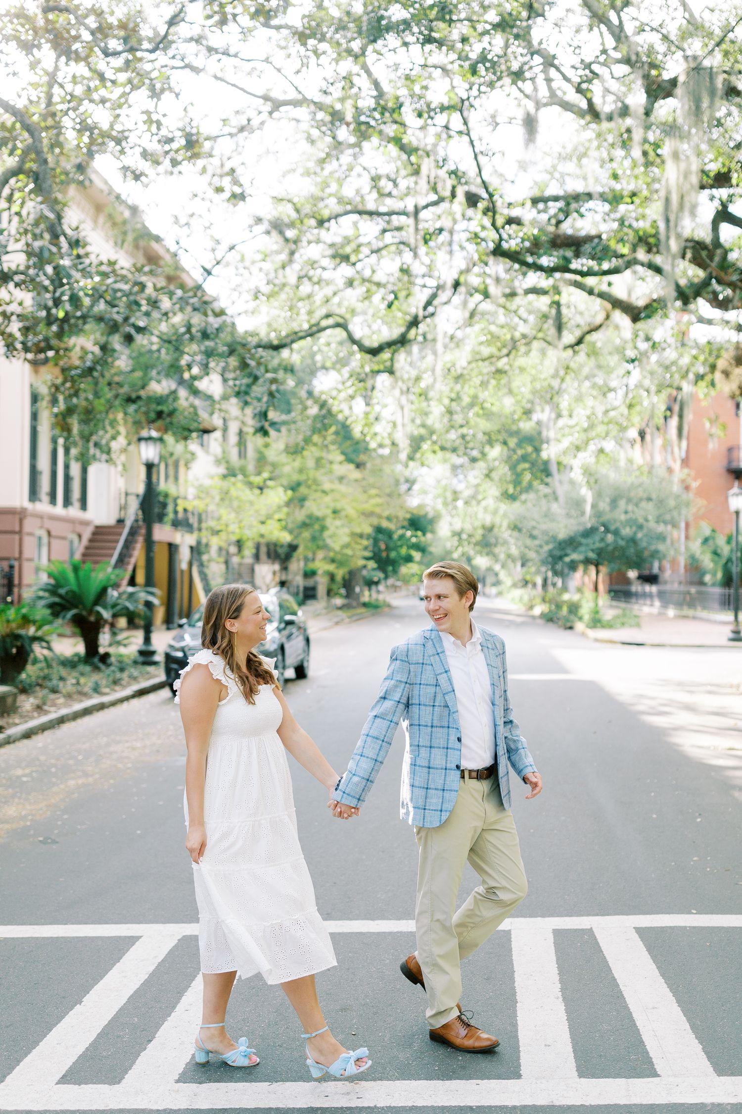A couple walks hand in hand across a crosswalk on a tree-lined street in Savannah, Georgia.