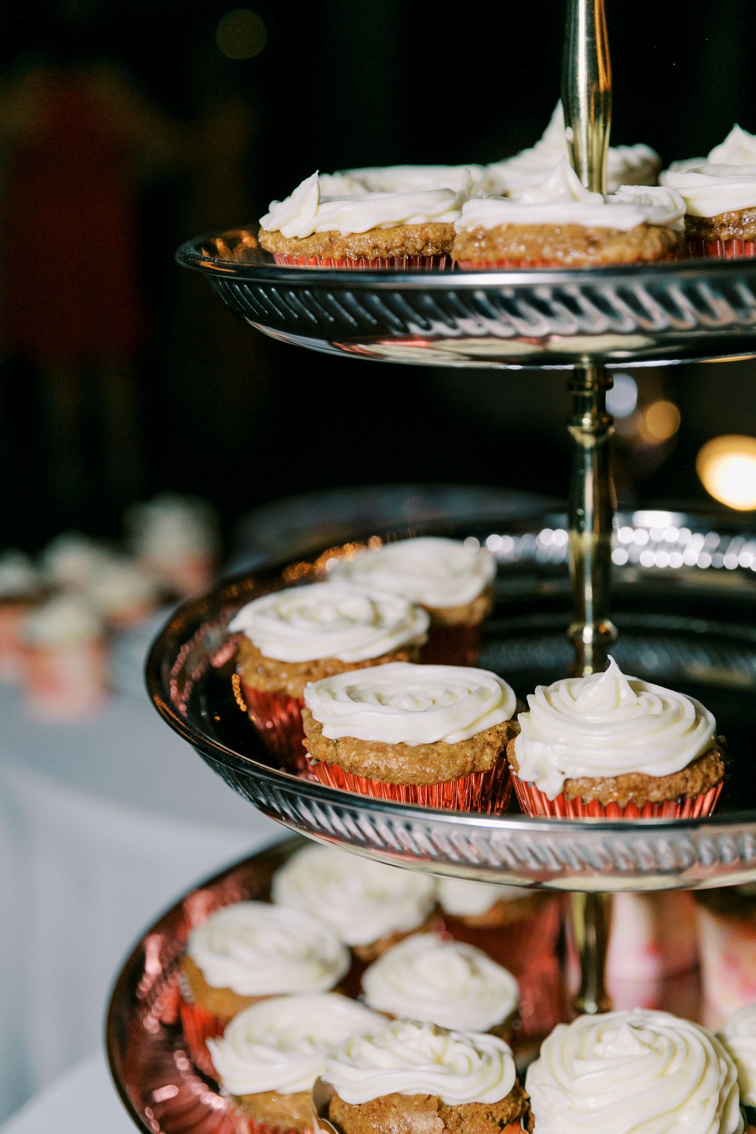 A tiered display stand of frosted cupcakes with white icing at an elegant event.