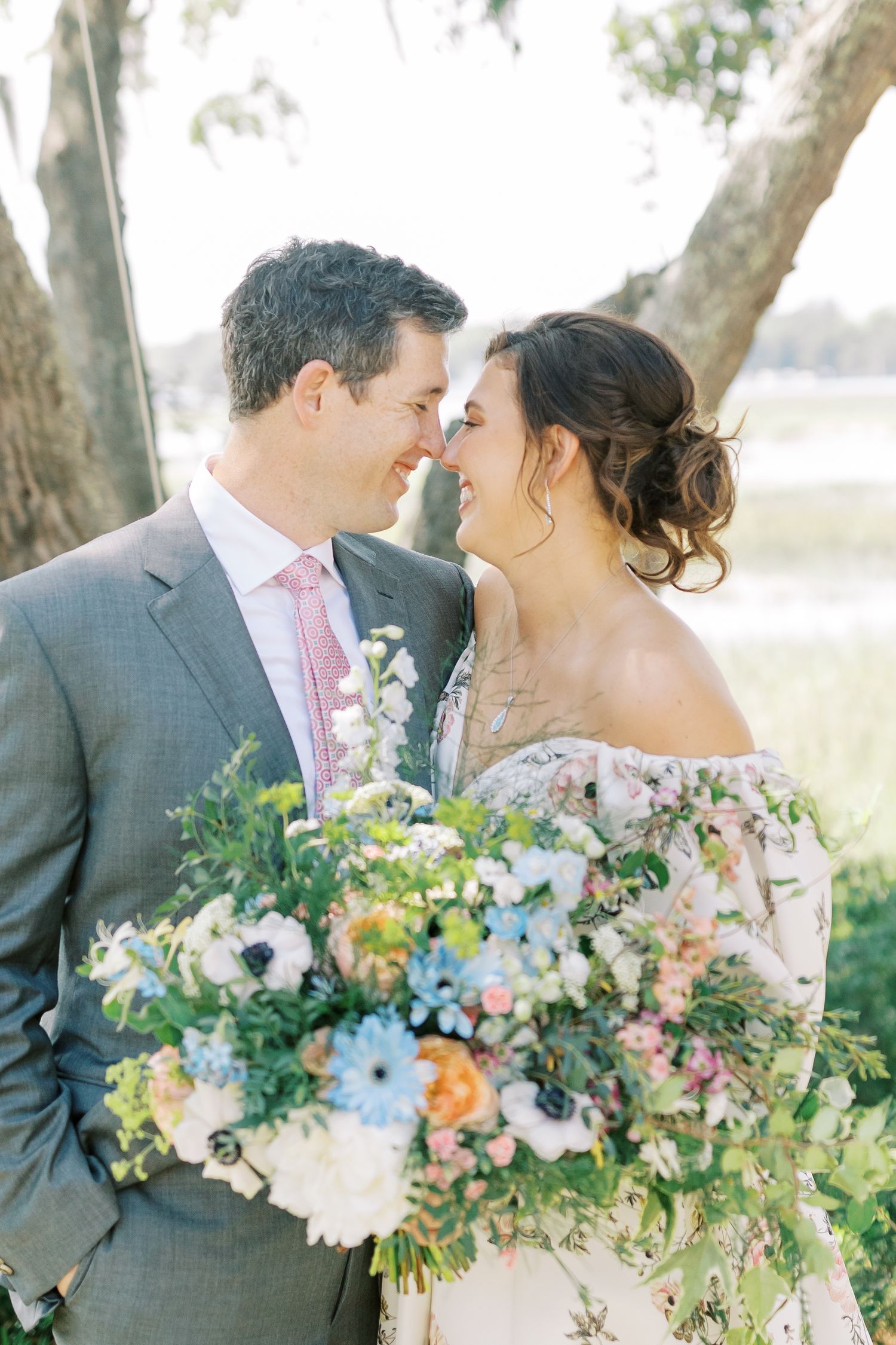 Wedding couple sharing an intimate moment with colorful bouquet under moss-draped trees.