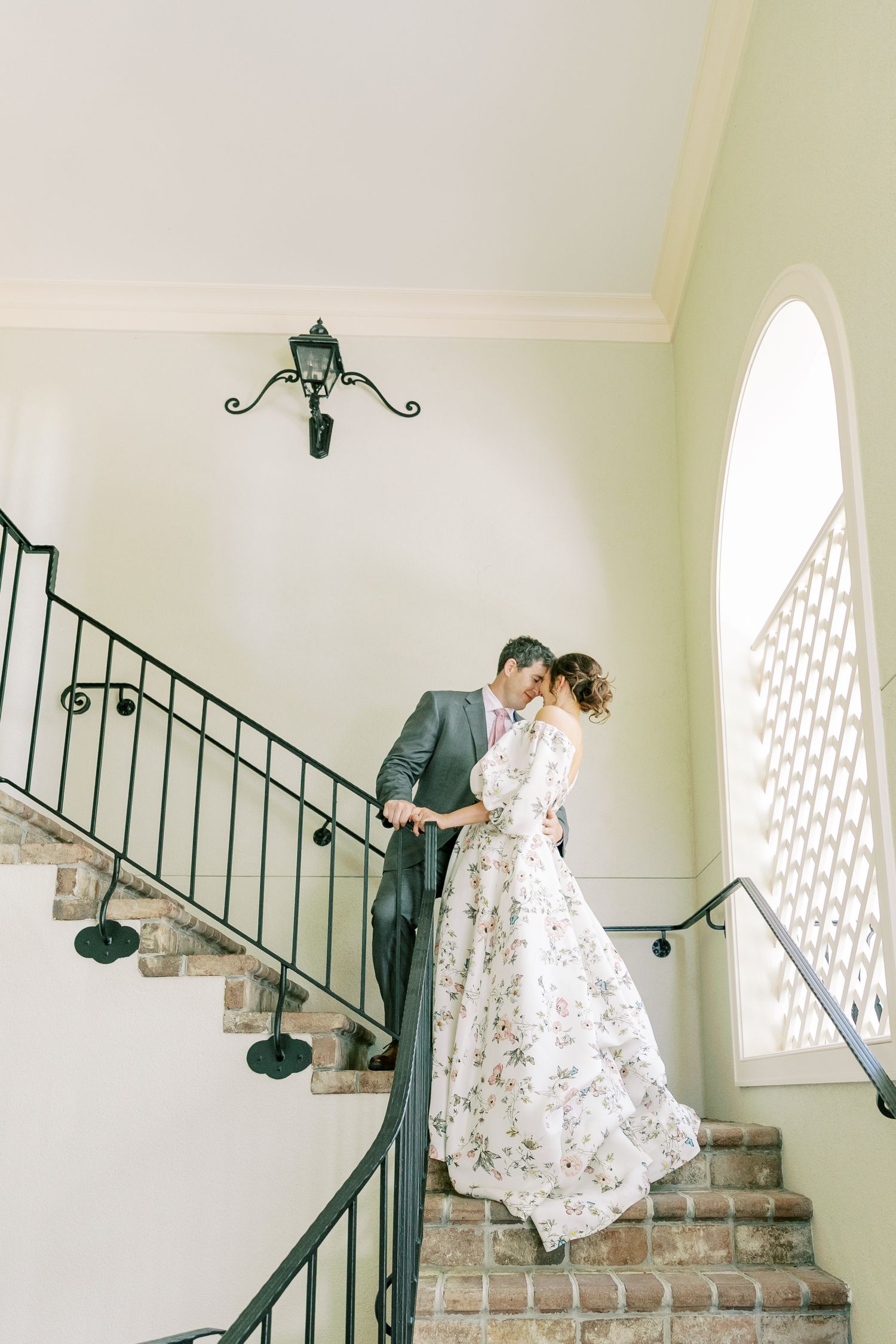 A graceful figure twirls on a brick staircase in an elegant white floral dress against bright interior walls.