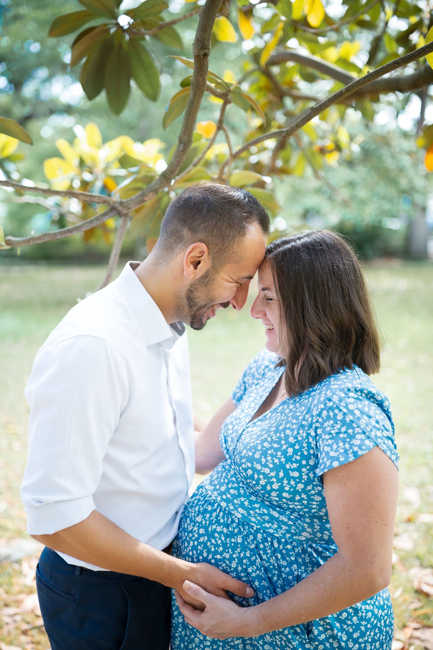 Sweet candid moments between an expecting couple under magnolia trees in a park.
