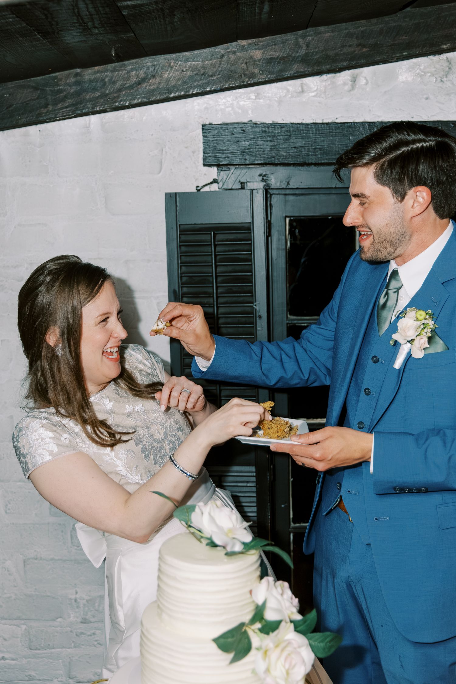 Newlyweds share cake during their wedding reception in a rustic indoor setting.