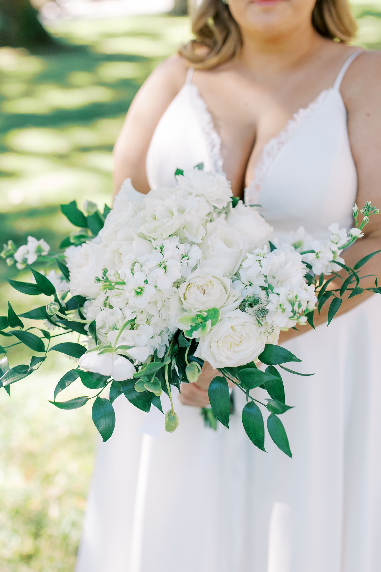 White floral wedding bouquet with roses, hydrangeas and green foliage against a white dress.