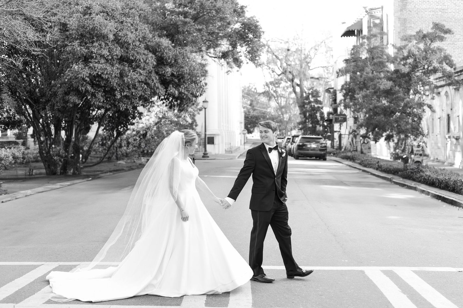 Wedding couple dancing playfully on a street between trees.