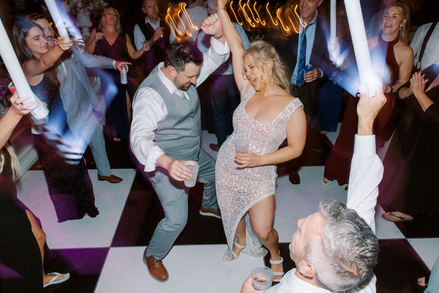 Wedding reception dance party with light-up foam sticks on black and white checkered floor.