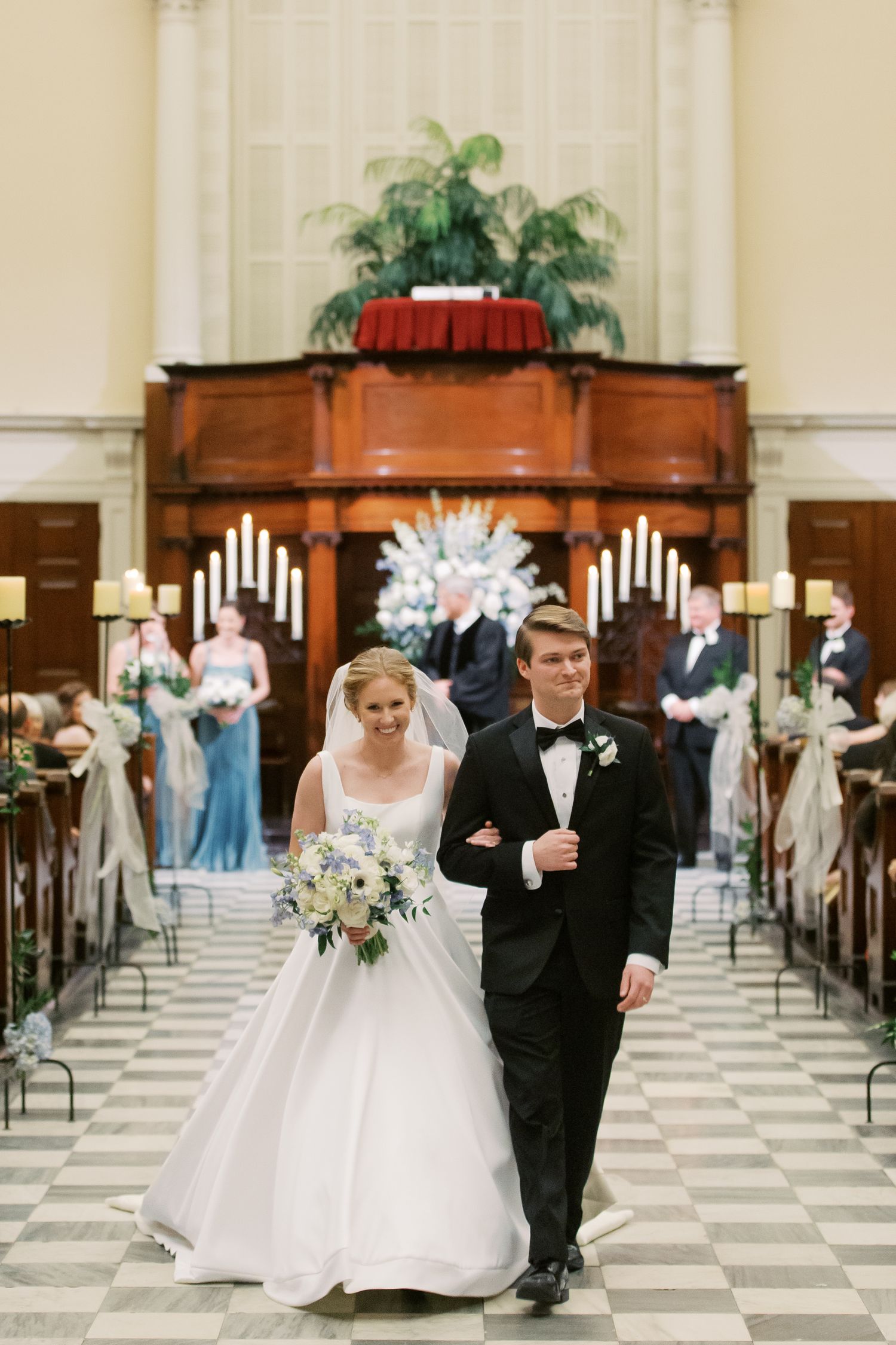 A traditional church wedding ceremony in a grand hall with checkered floors and wooden pews.
