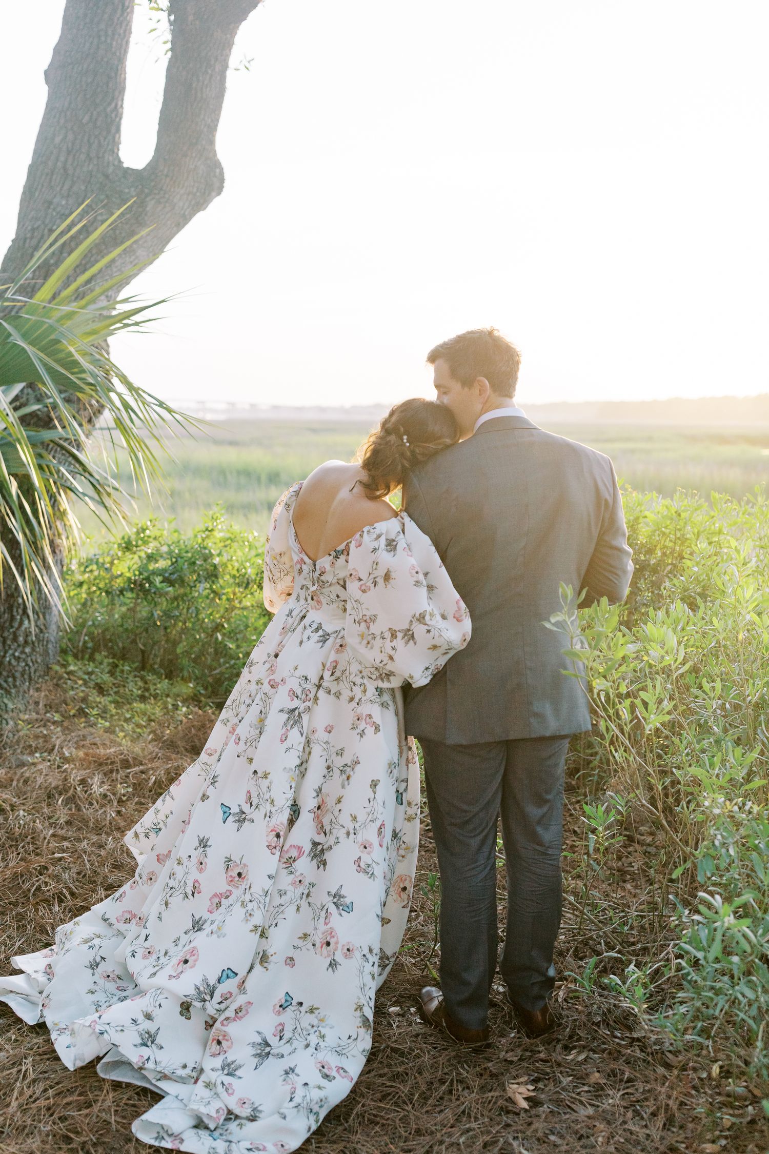 A couple embraces while looking out over a scenic marsh landscape at sunset.