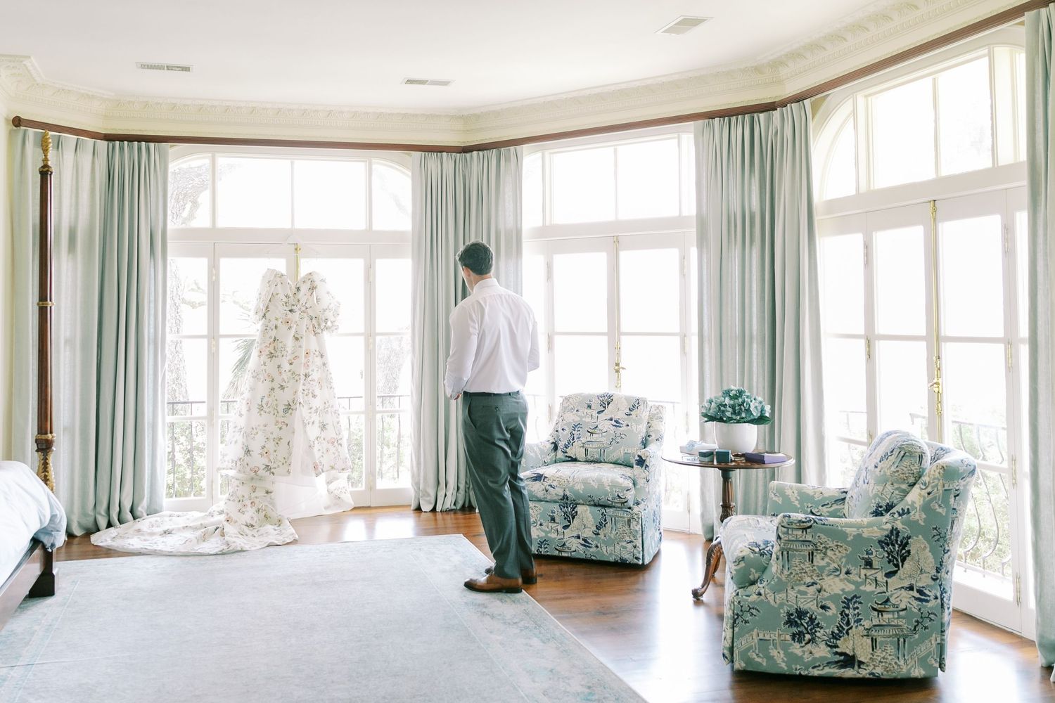Person standing in bright corner room with mint green curtains, floral armchairs and white Christmas tree.