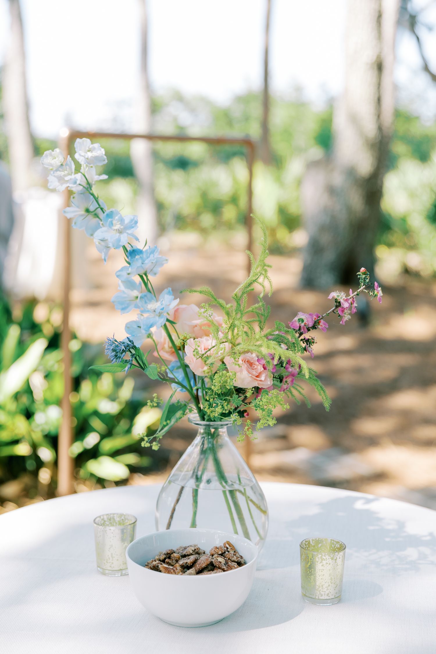 Delicate blue and pink flowers arranged in small glass vases on a white table for an elegant garden party setting.
