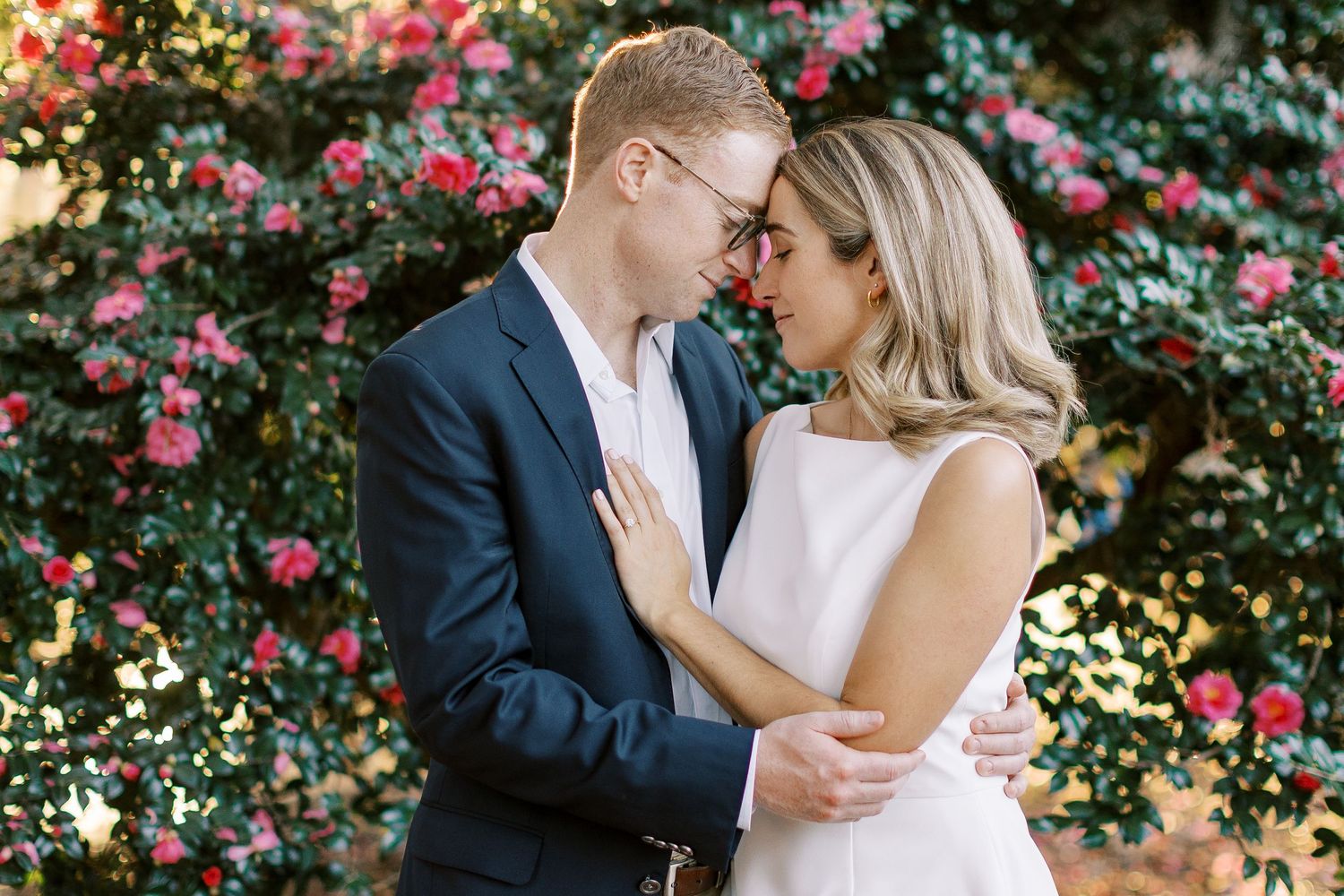 A romantic couple shares tender moments in front of a blooming pink rose garden on their wedding day.