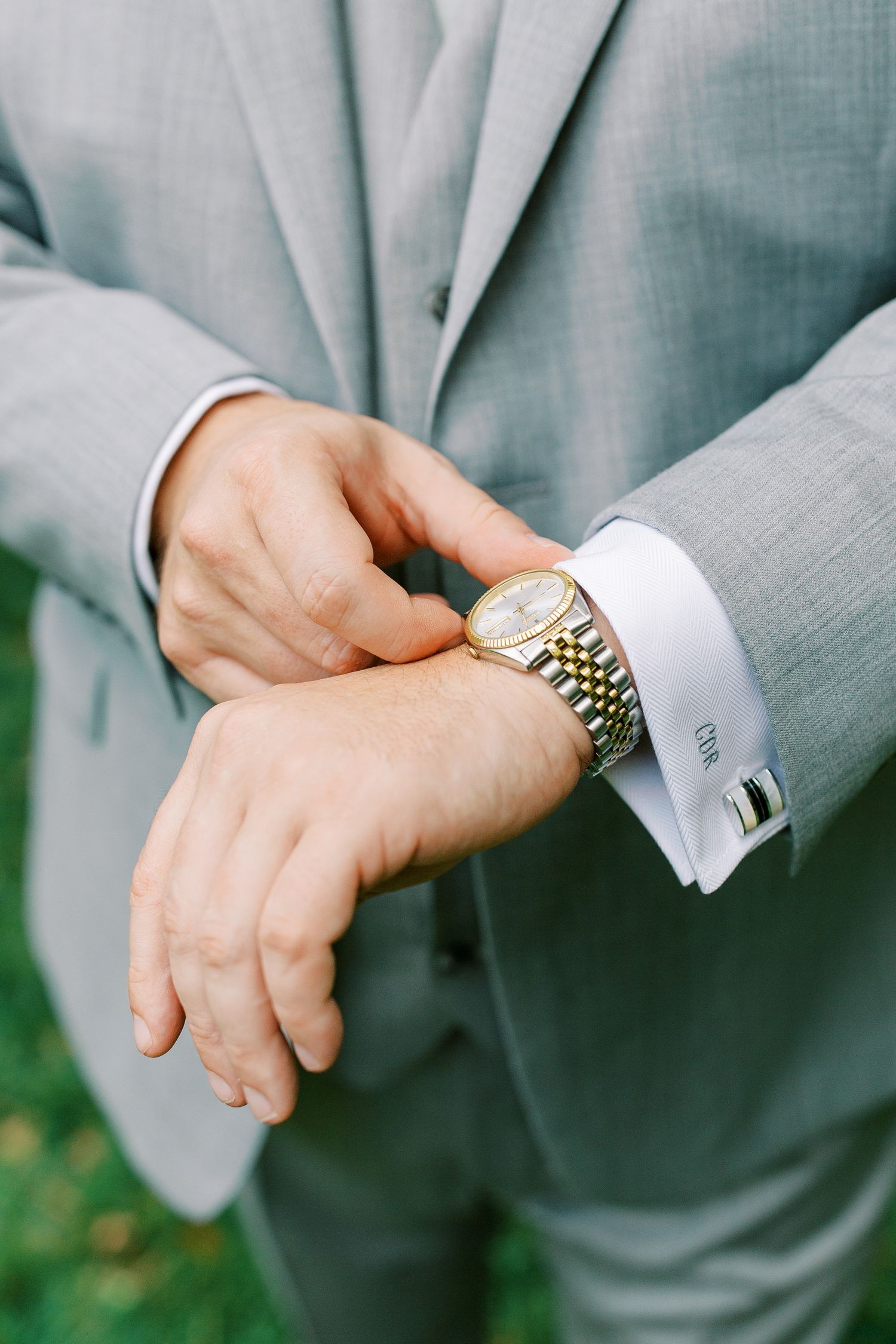 Close-up of groom's hands adjusting two-tone watch with silver cufflinks.