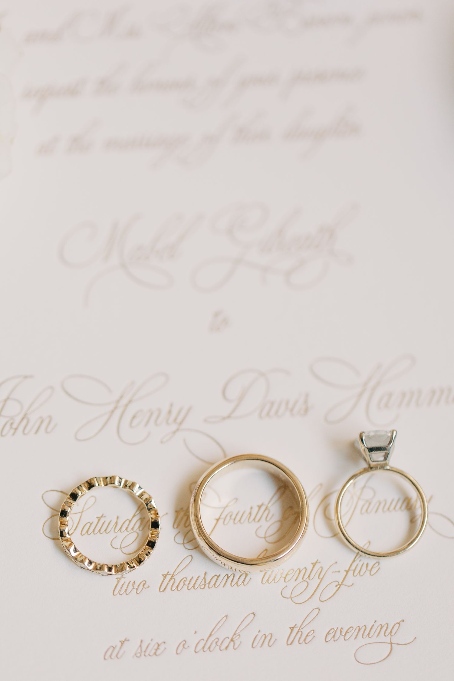 Wedding rings and engagement ring displayed on white paper with elegant calligraphy.