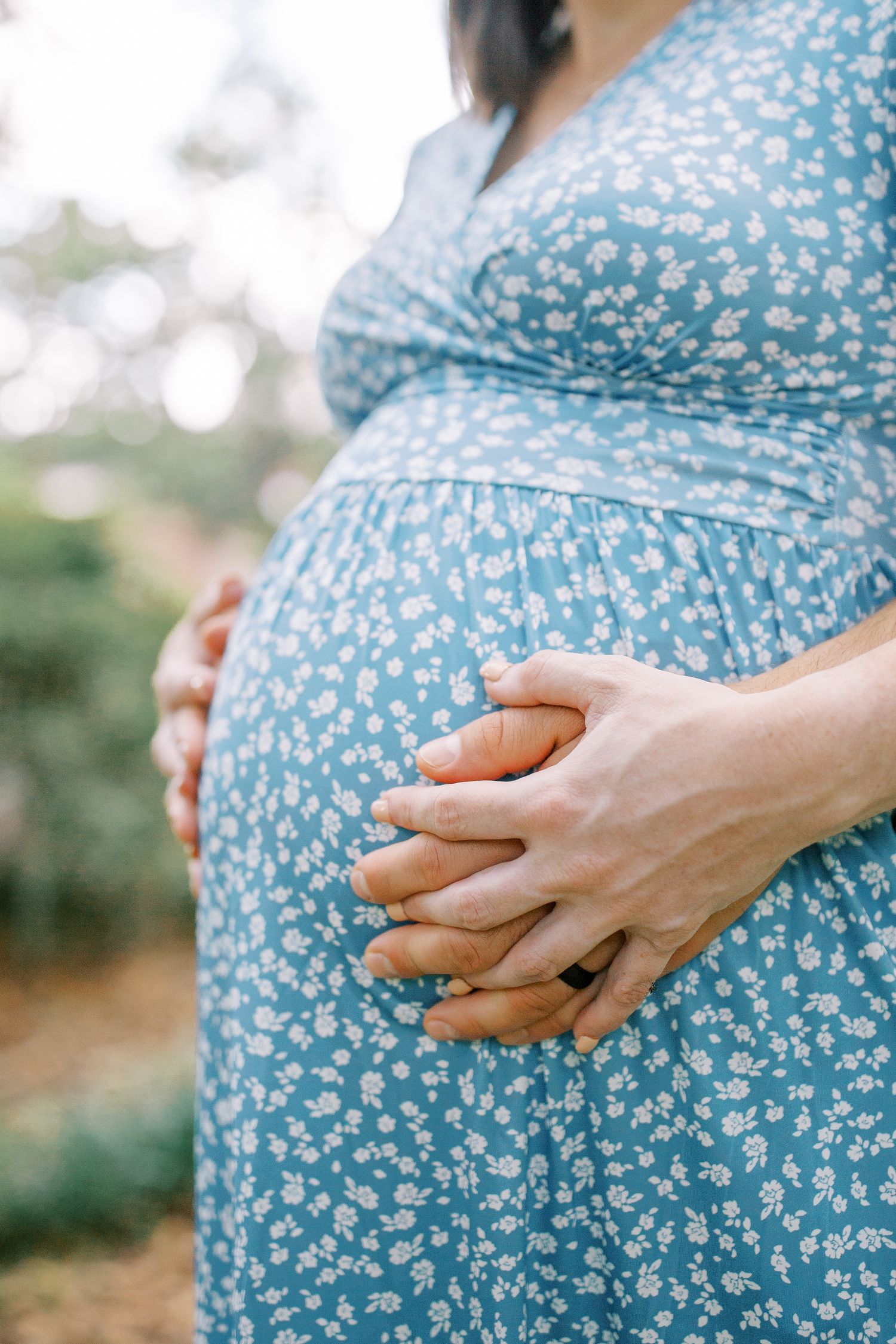 Close-up shots of hands gently cradling a pregnant belly in a blue floral dress.